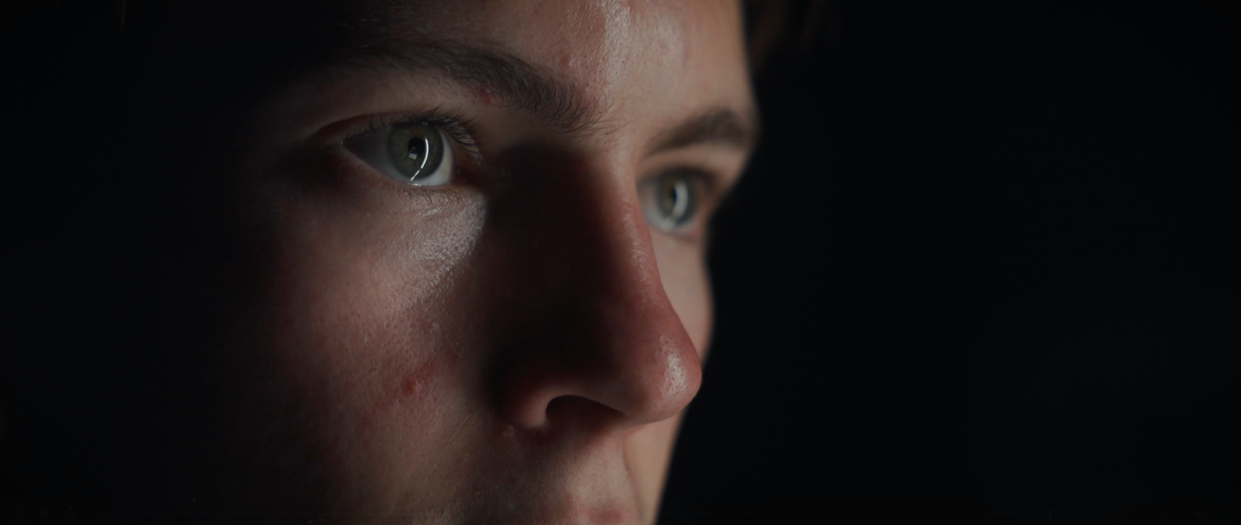 Close-up of a person's face, showing their blue eyes and part of their nose, with dramatic lighting on one side and a dark background.