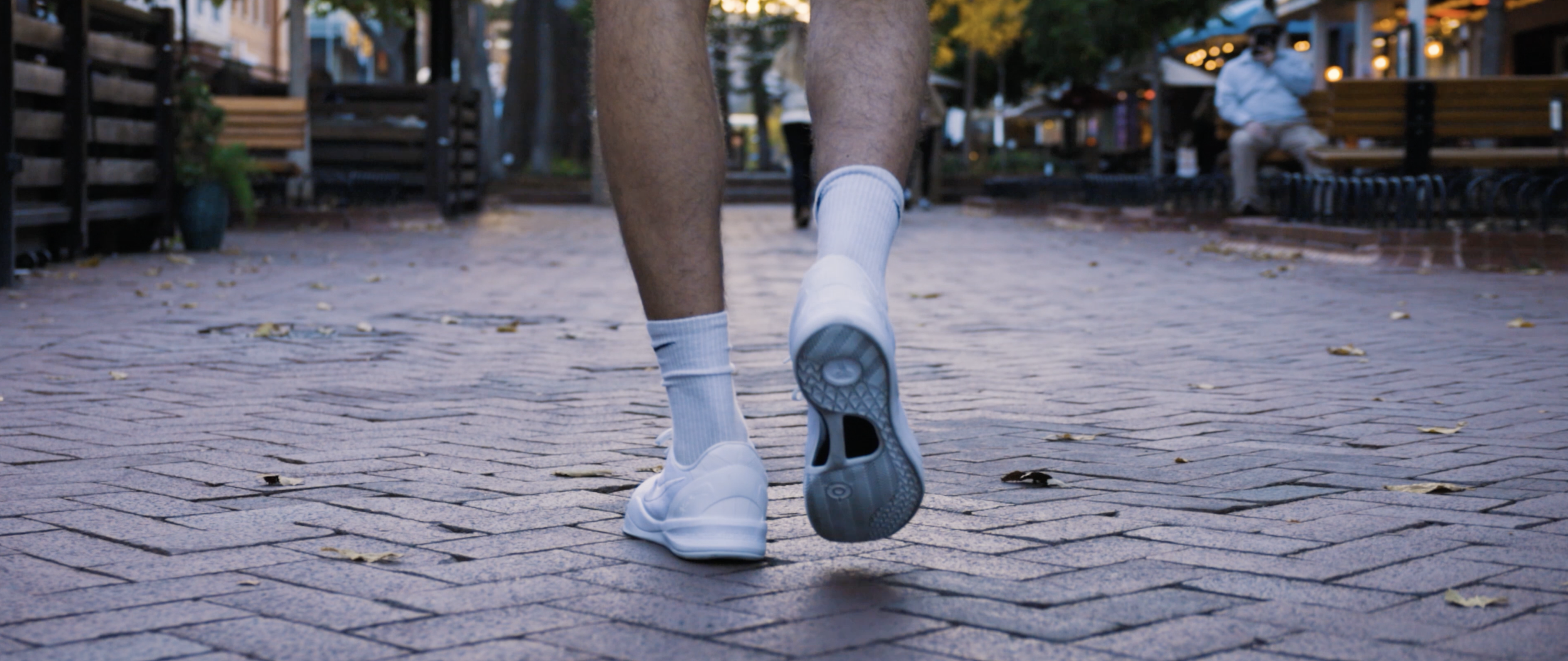 Close-up of a person jogging on a paved outdoor sidewalk, focusing on their legs and white athletic shoes.