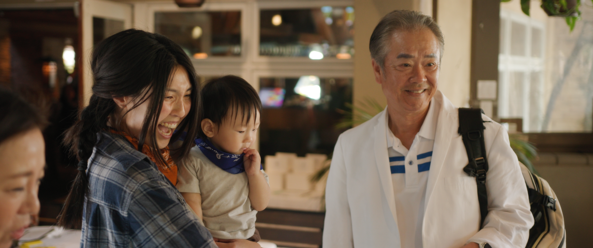 A family of four, including an elderly man, a woman, and two children, are smiling and interacting at a restaurant or cafe.