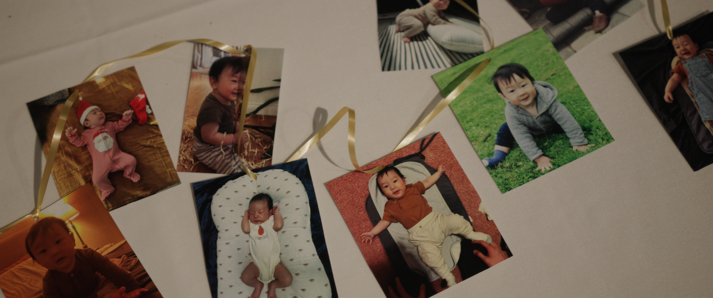 Collection of six baby and toddler photographs spread out on a white surface, decorated with golden ribbons.