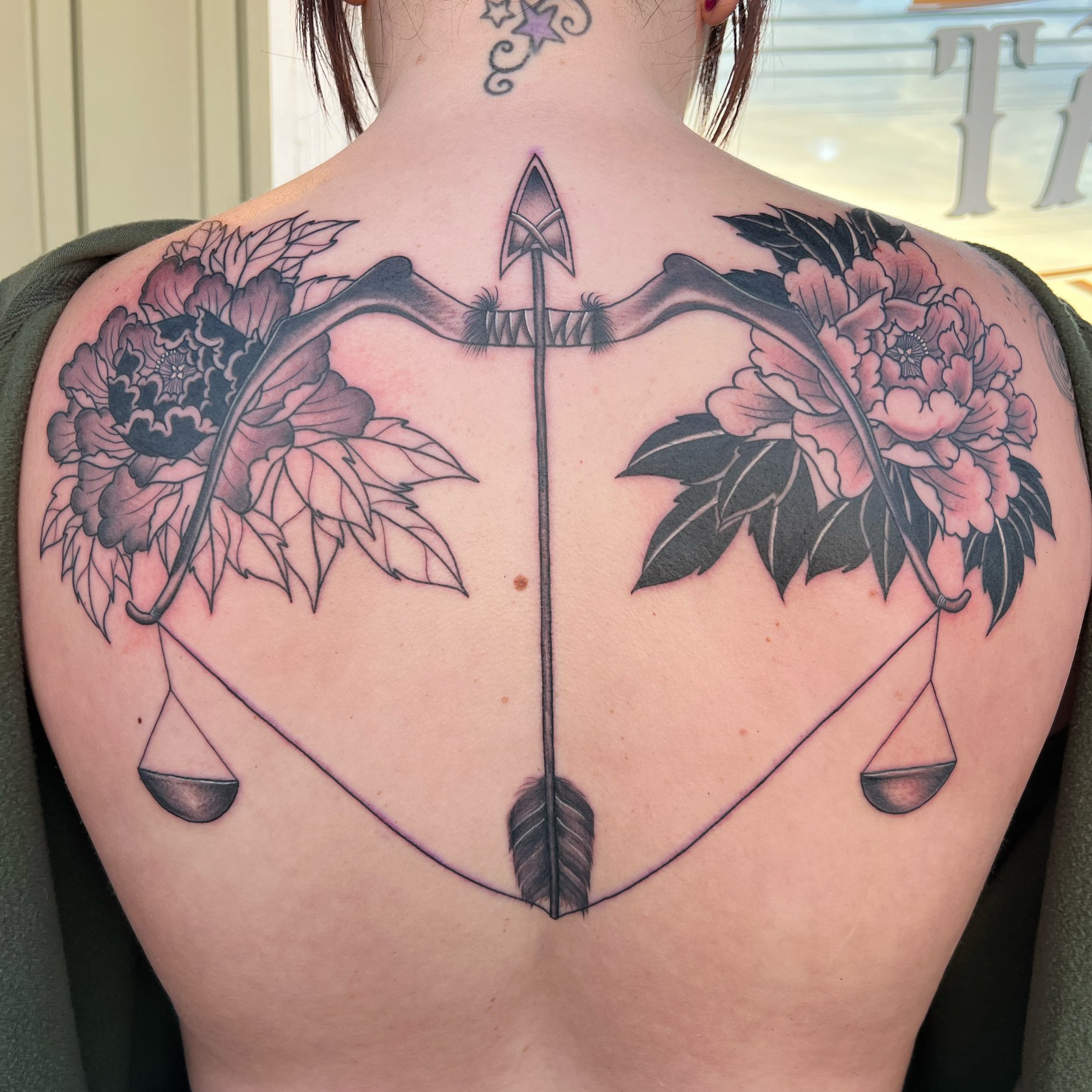 Tattoo of a bow and arrow with floral details on the back.