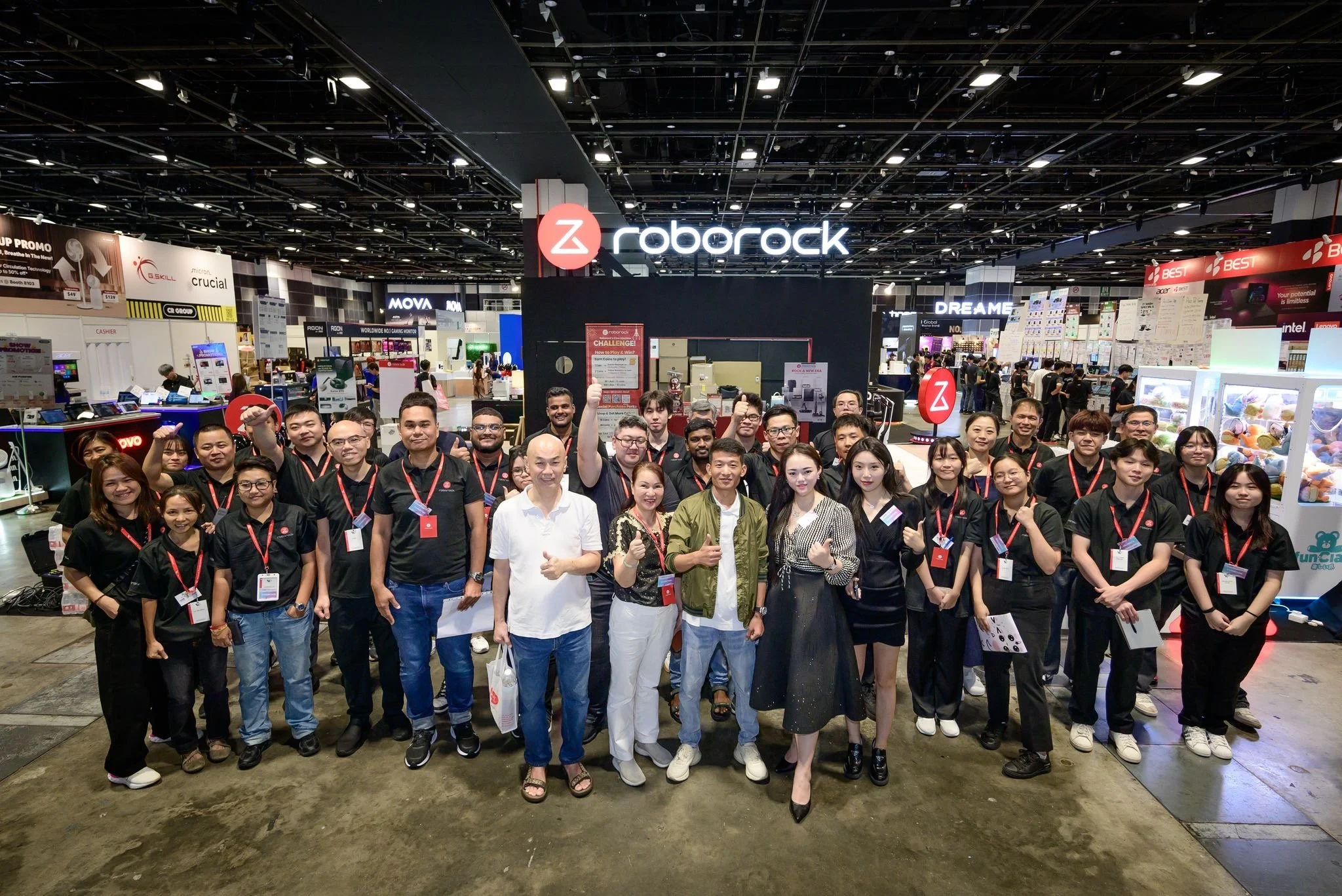Group of people posing for a photo at a technology trade show, with booths and electronic displays in the background, including the Roborock logo.