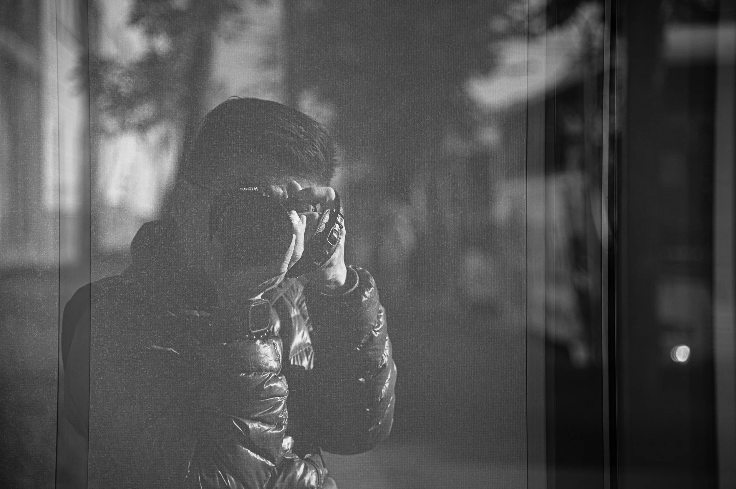 Person taking photograph through glass reflection in black and white.