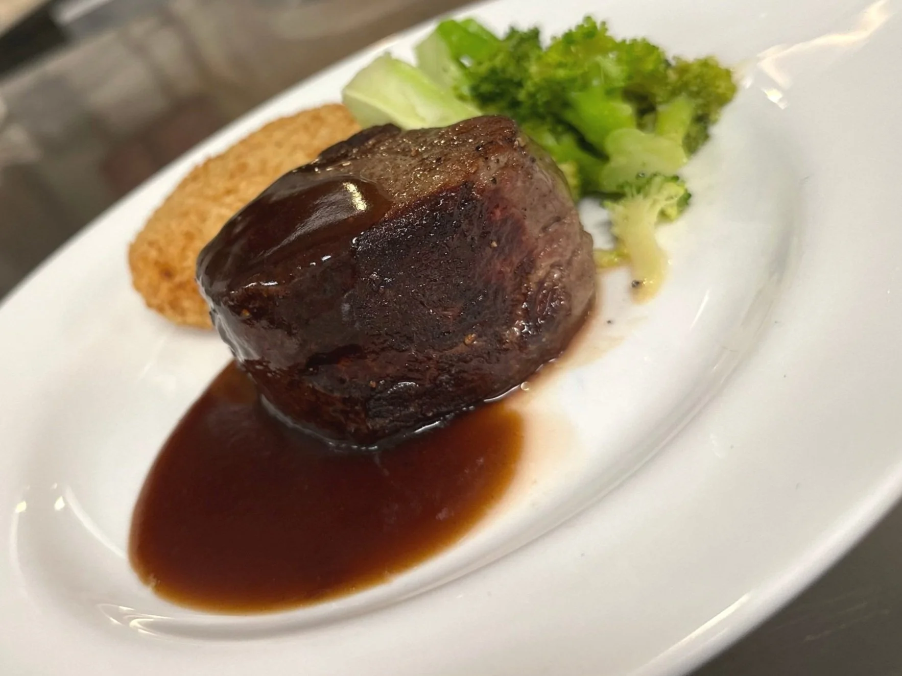 Meatloaf with brown gravy, served with broccoli and a breaded fried item on a white plate.