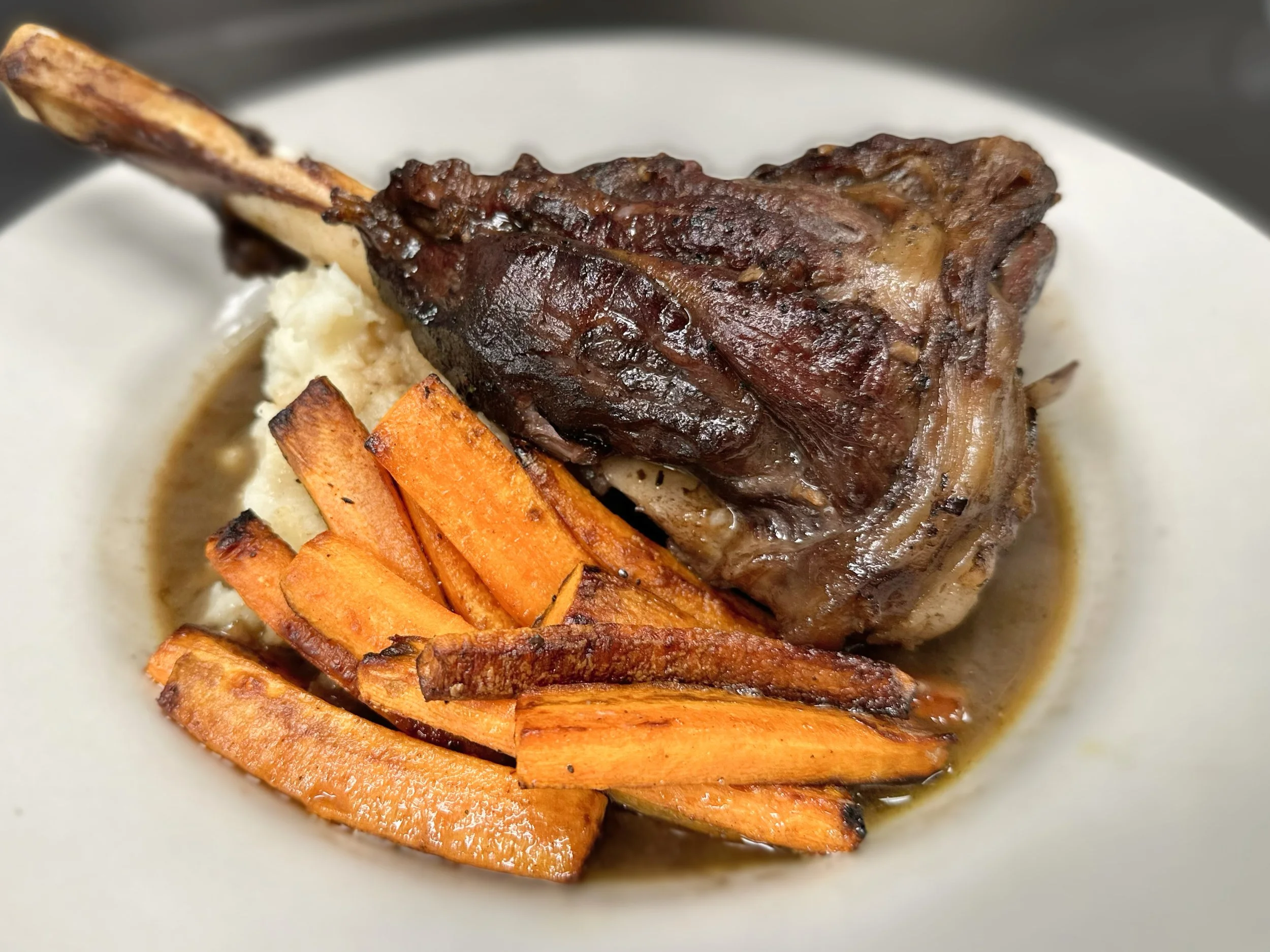 Roasted lamb shank with roasted sweet potatoes on a white plate.