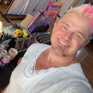 Chis Holmes and pink-streaked hair takes a selfie in a room filled with makeup, beauty productsm,candles and wax melts.