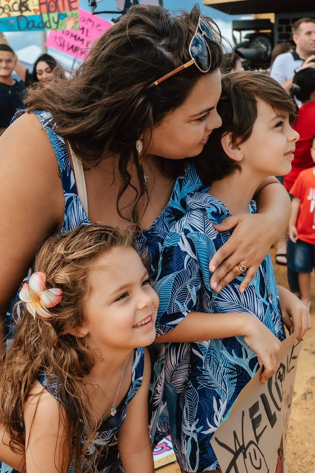A woman with two young girls at a family-friendly outdoor event, holding a sign and smiling. San Antonio Military Homecoming Photographer