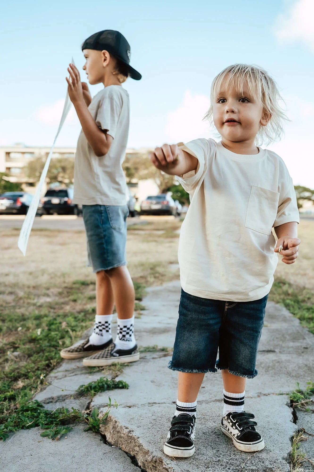 Two young boys standing on a sidewalk outdoors. The boy in the foreground points with his finger, wearing a white t-shirt, dark shorts, and black sneakers. San Antonio Military Homecoming Photographer