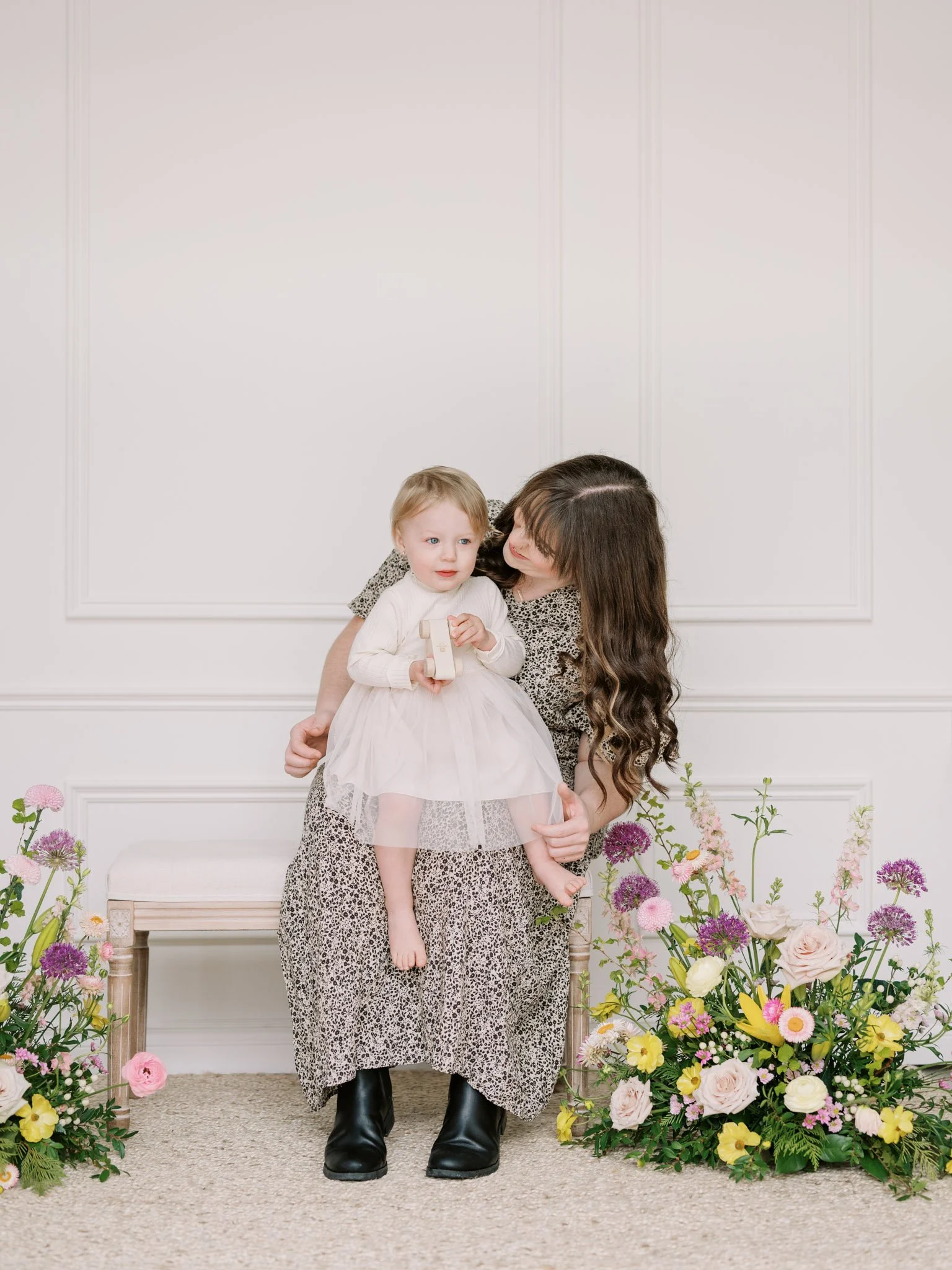 Woman sitting with a child on her lap, surrounded by floral arrangements indoors.
