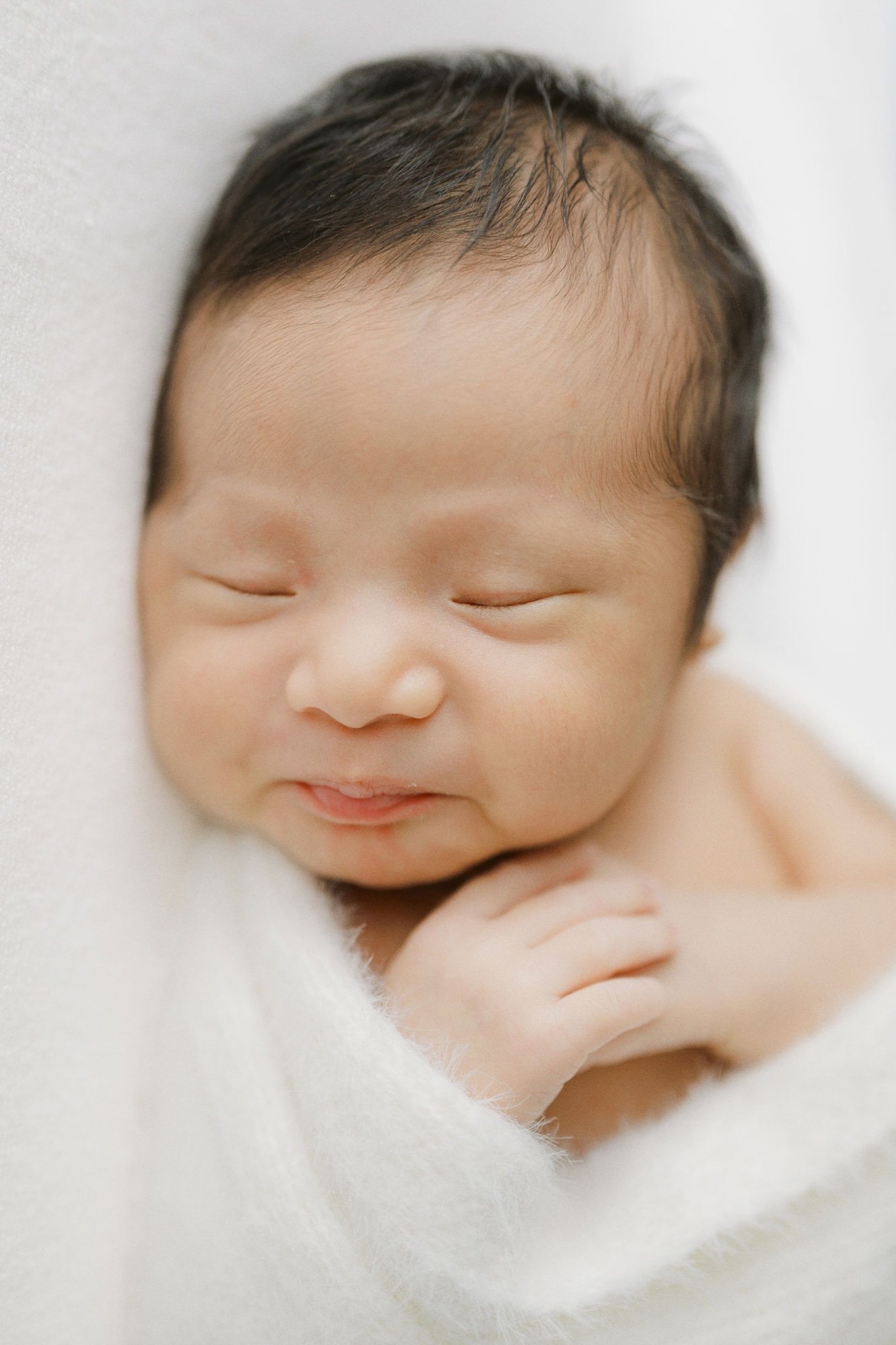 Close-up of a smiling baby with closed eyes, wrapped in a white blanket