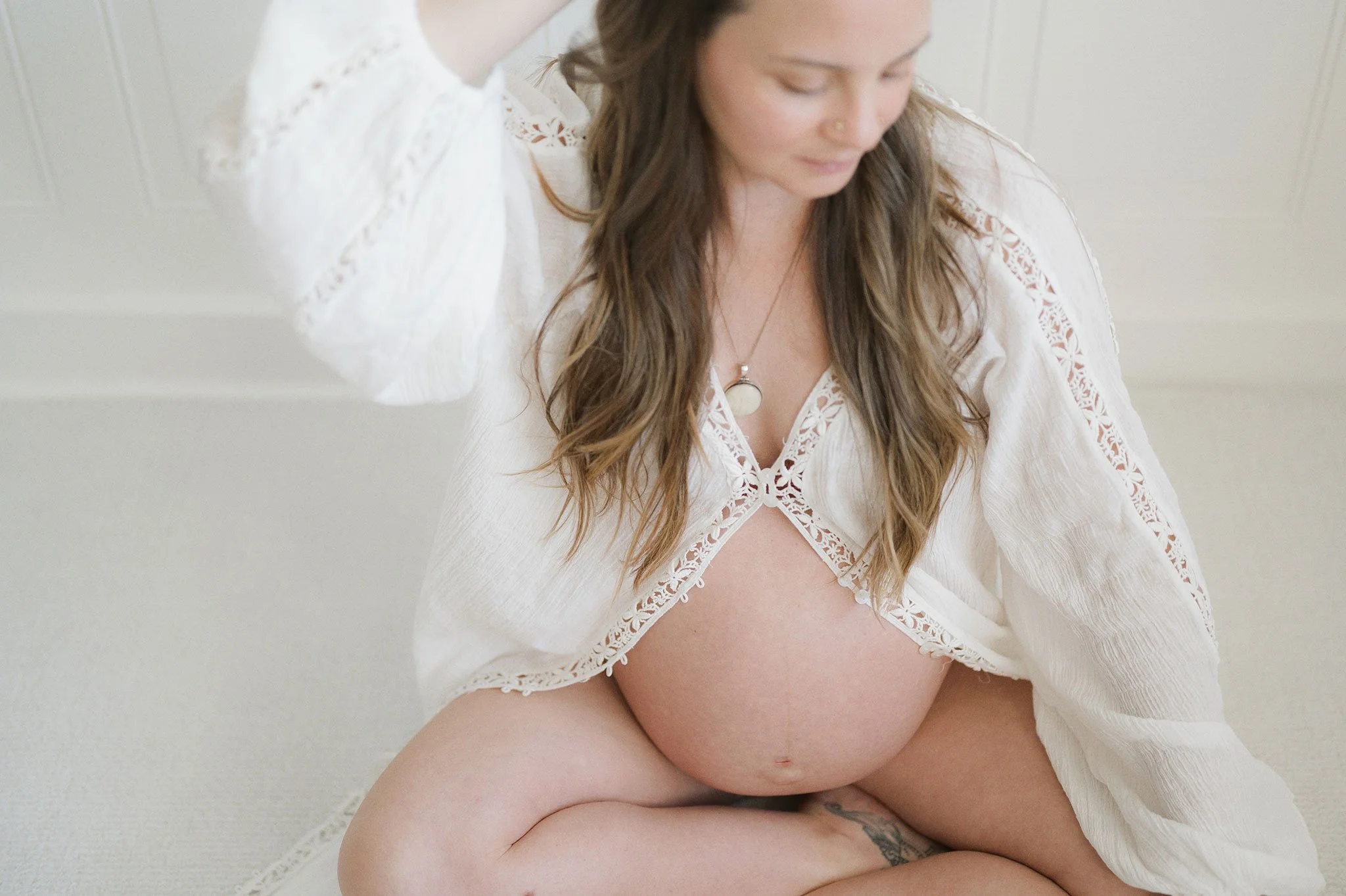 Pregnant woman sitting cross-legged wearing a white lace robe.