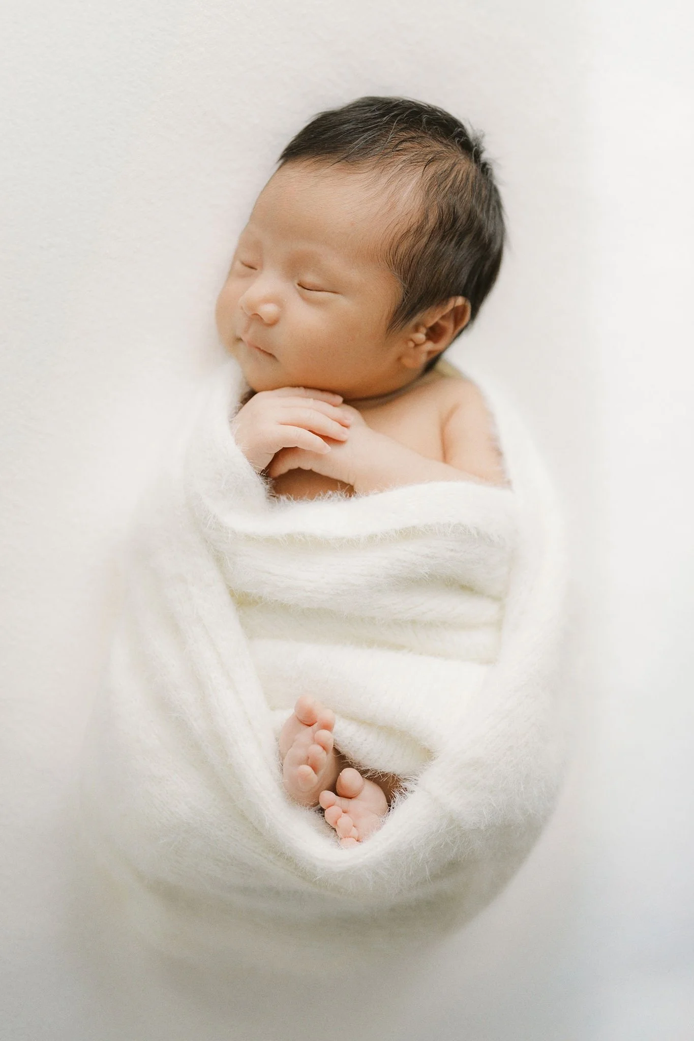 A sleeping newborn wrapped in a soft white blanket.