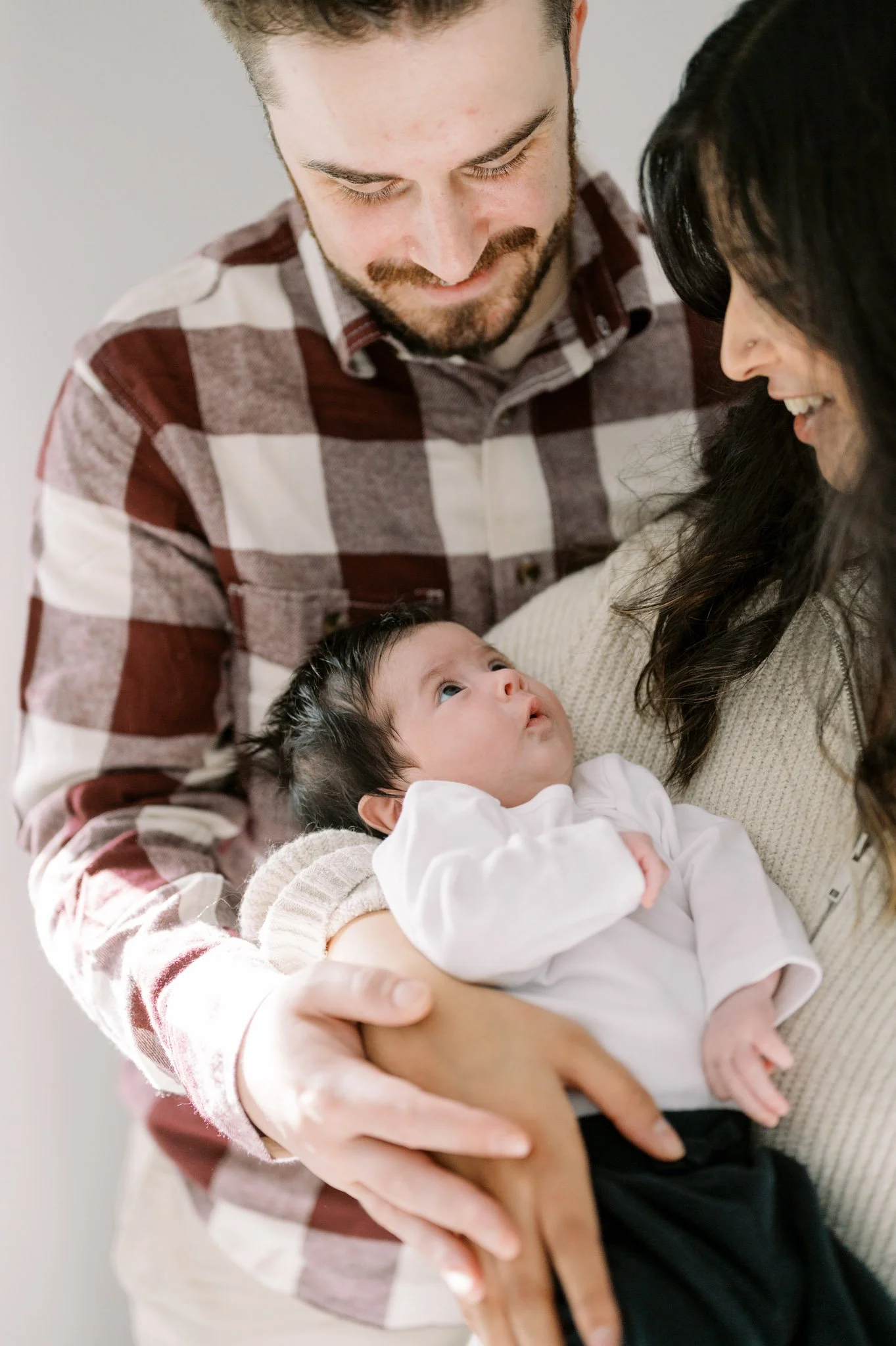 Parents holding their newborn baby, smiling at the infant.