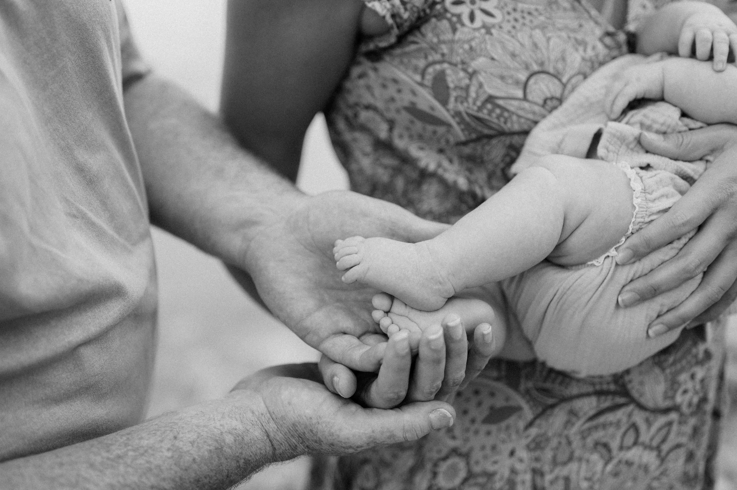 Black and white photo of adult hands holding a baby's feet.