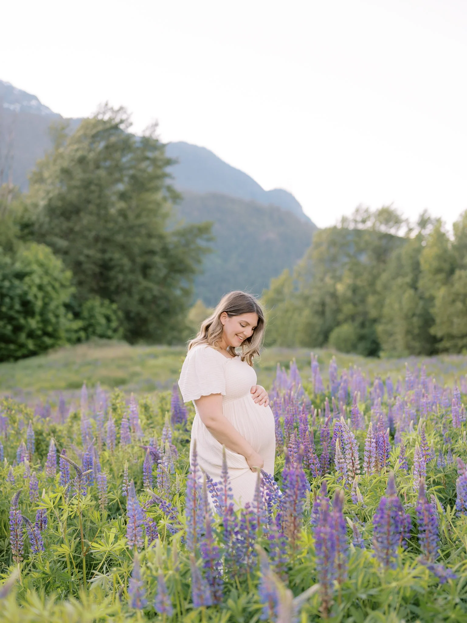 Pregnant woman in white dress among purple wildflowers