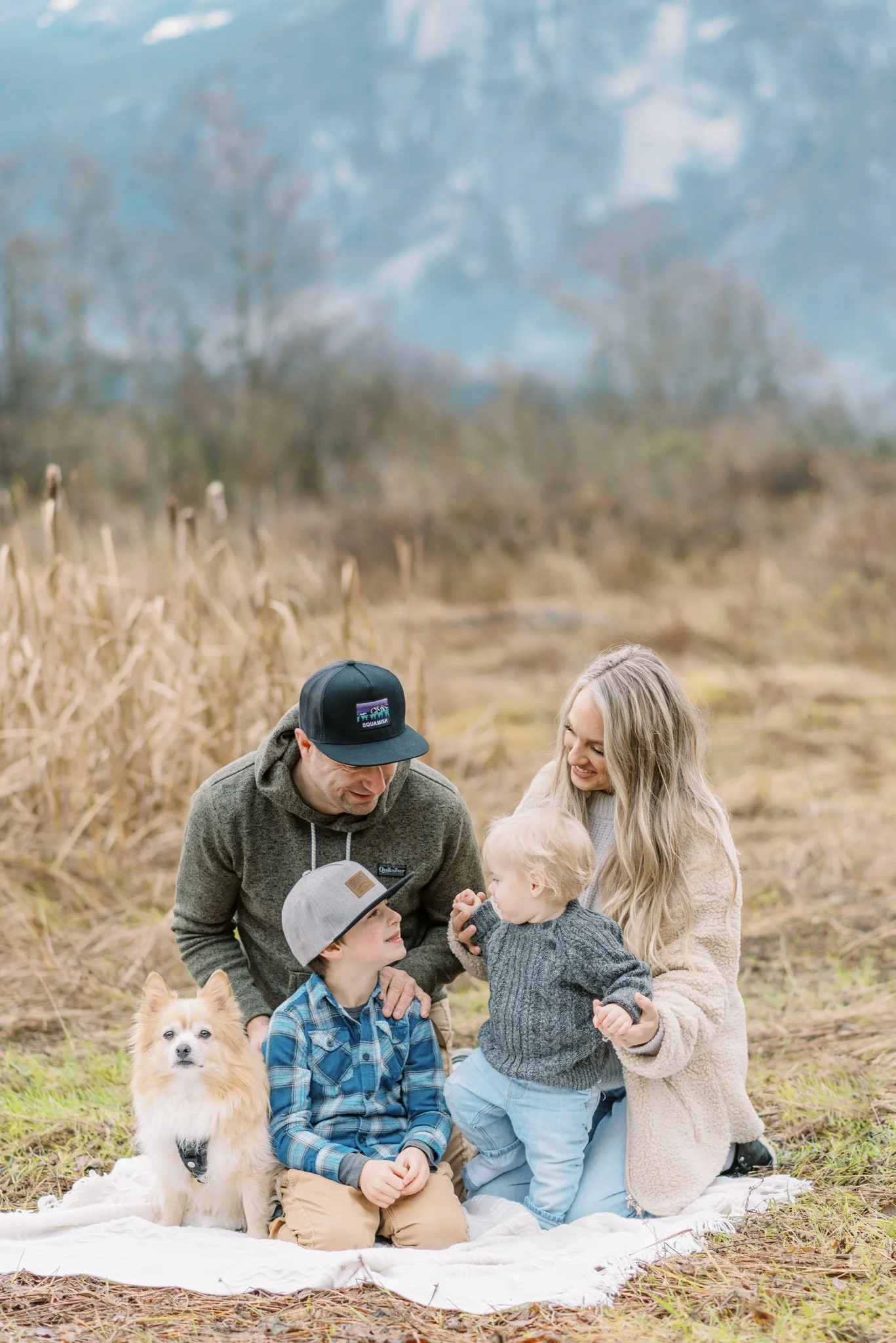 family with dog sitting on blanket smiling at each other