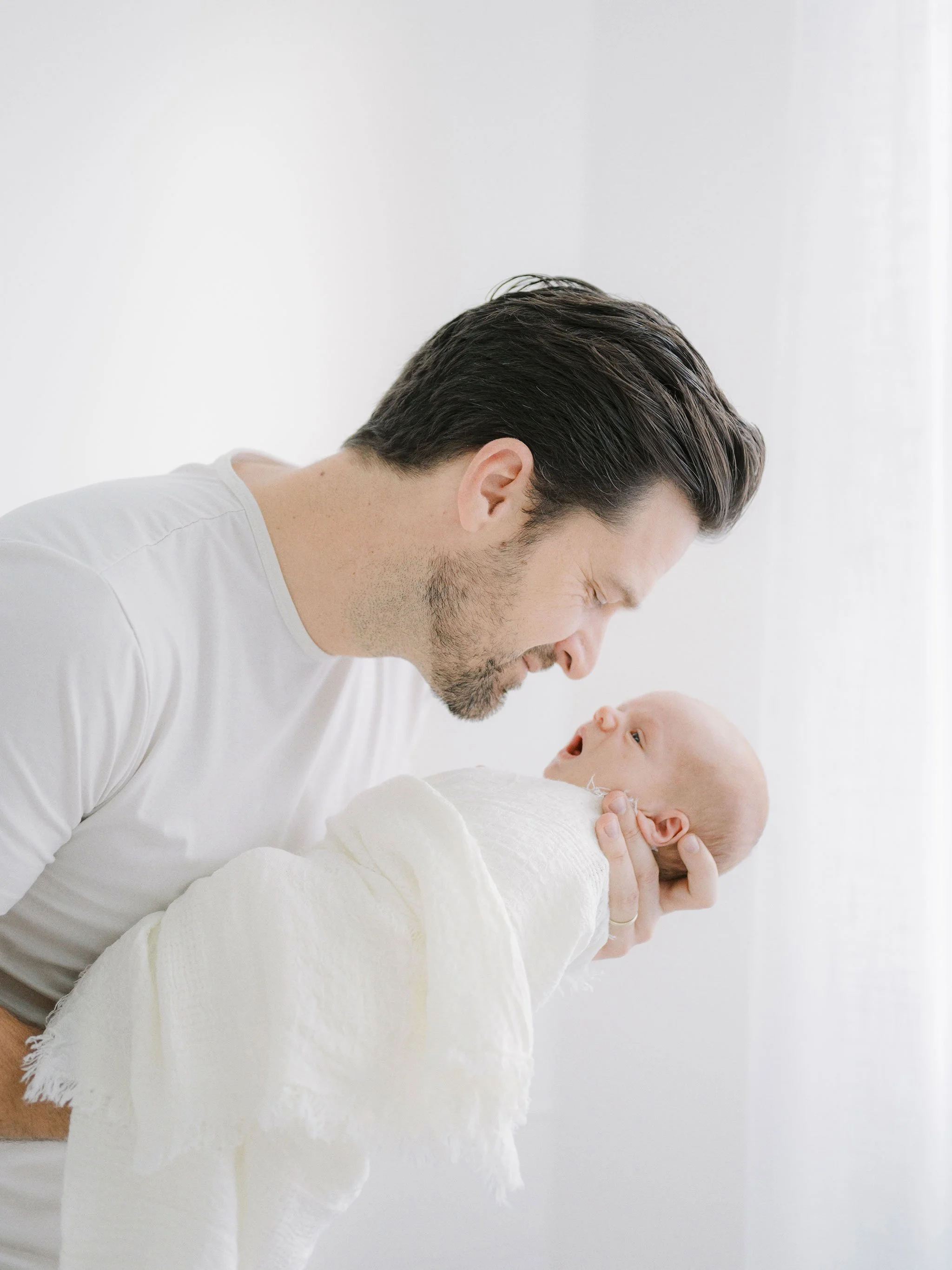 Man in white shirt holding and smiling at a swaddled newborn baby