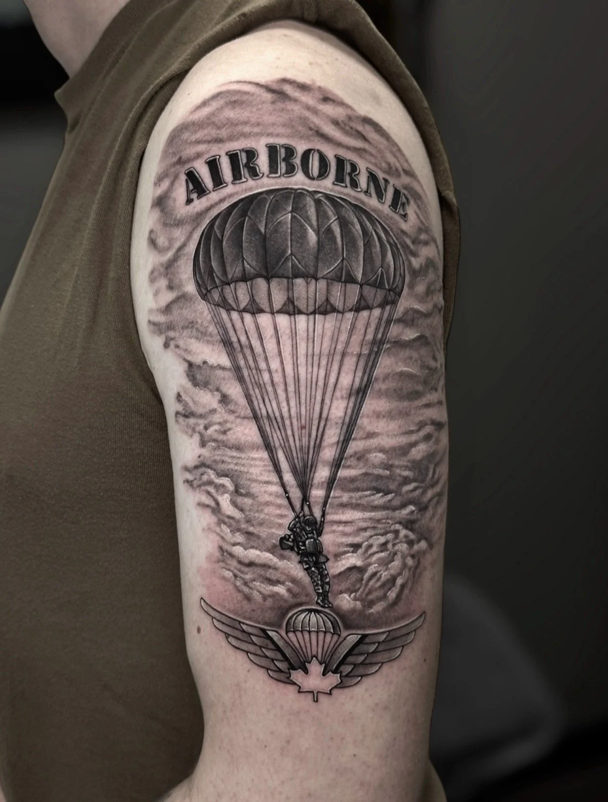 Black and grey Airborne tattoo with a parachutist, clouds and Canadian parachute wings, by Chris Kennedy.