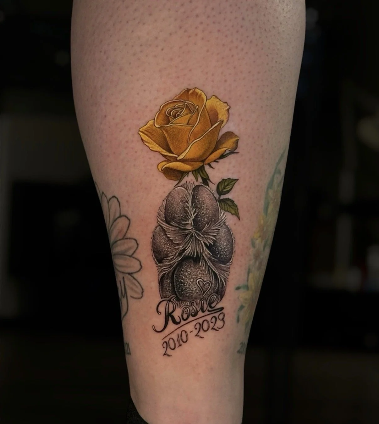 Memorial paw print and yellow rose tattoo with the name Rosie, by Chris Kennedy.