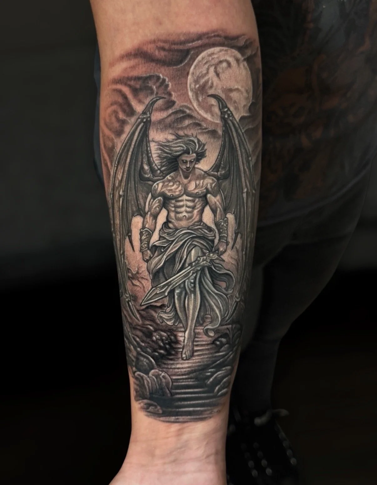 Black and grey winged warrior tattoo with a sword, moon and rocky path, by Chris Kennedy.