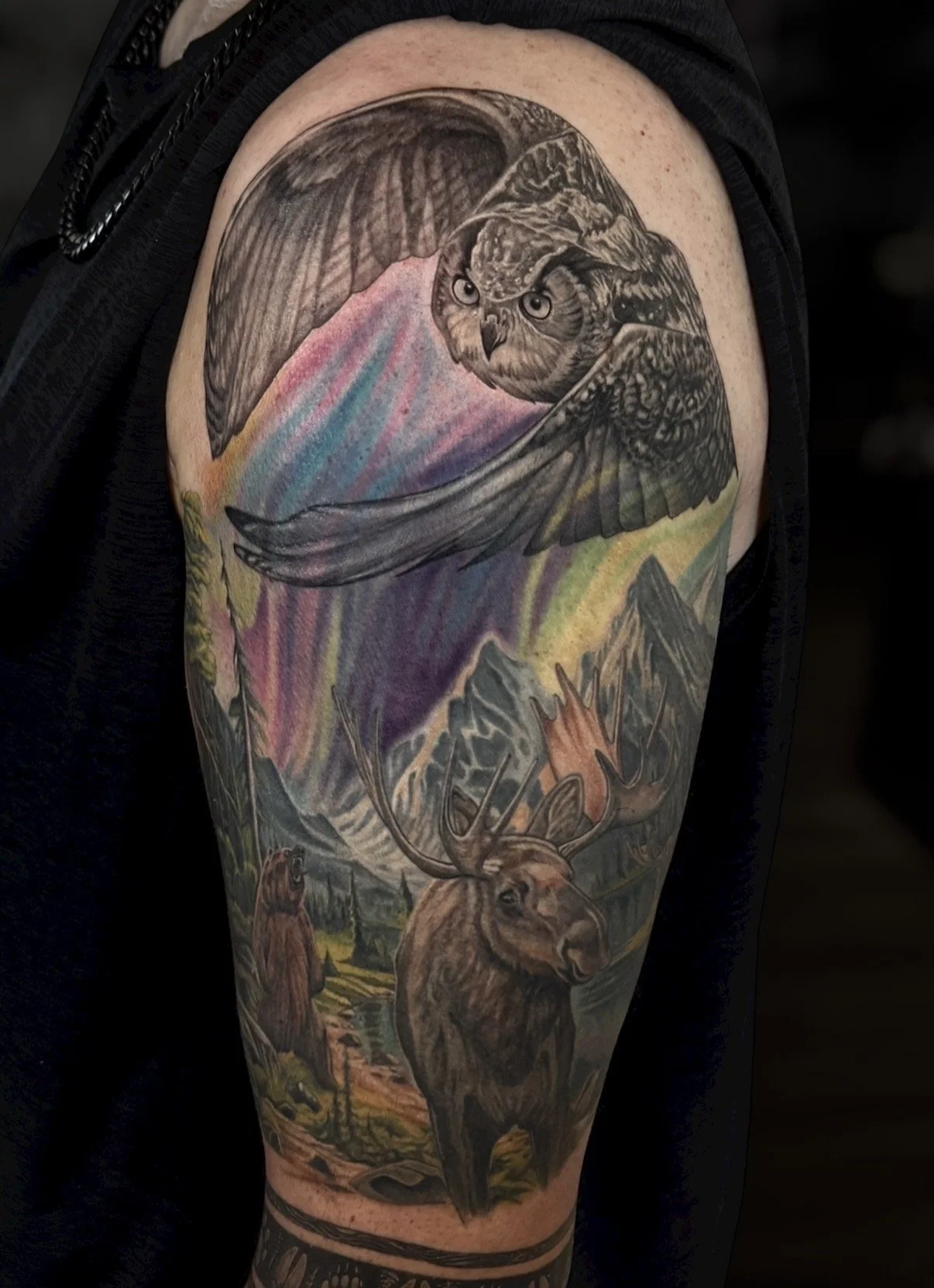 Wildlife sleeve tattoo with an owl, moose, mountains and northern lights, by Chris Kennedy.