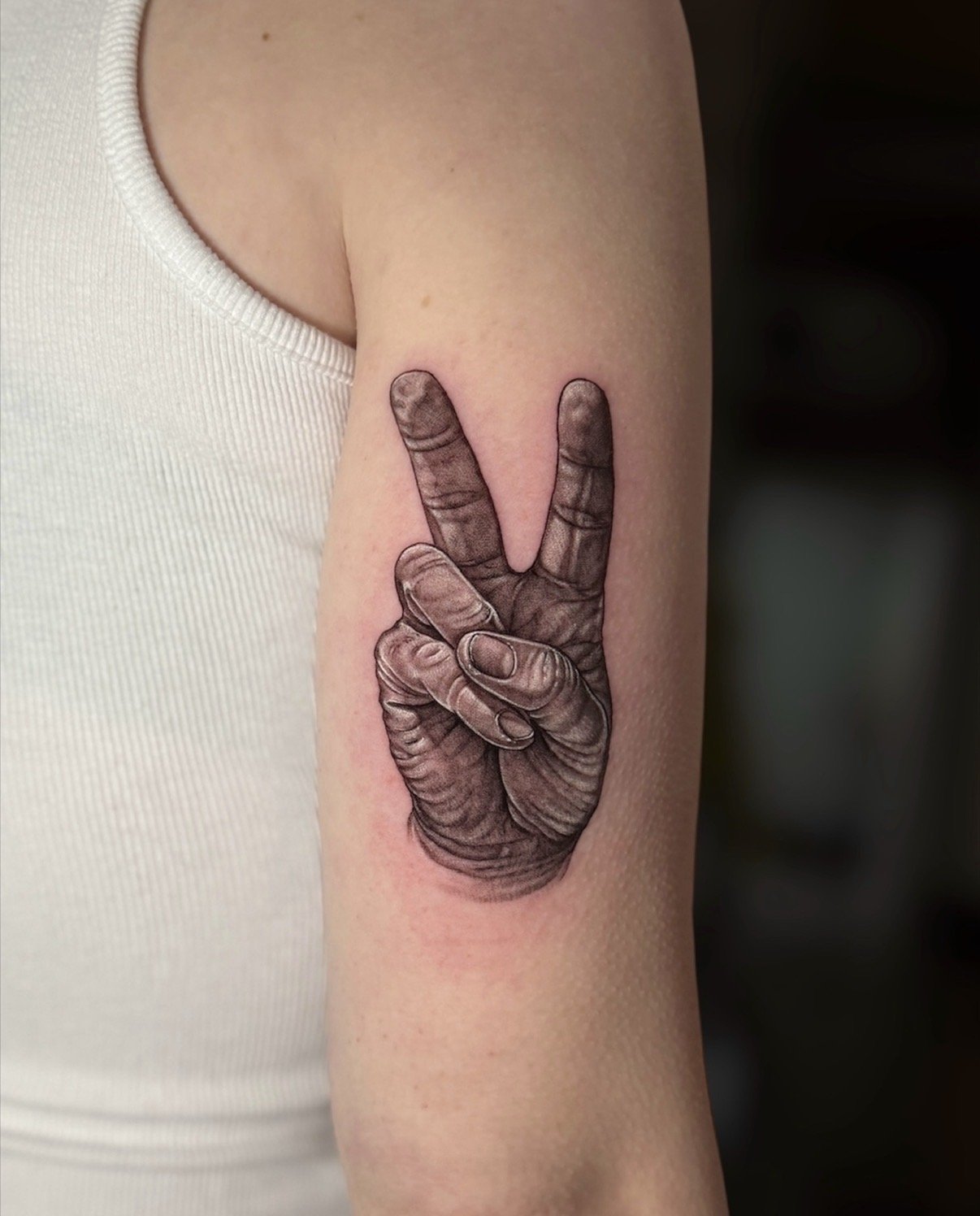 Black and grey realistic hand tattoo making a peace sign, by Chris Kennedy.