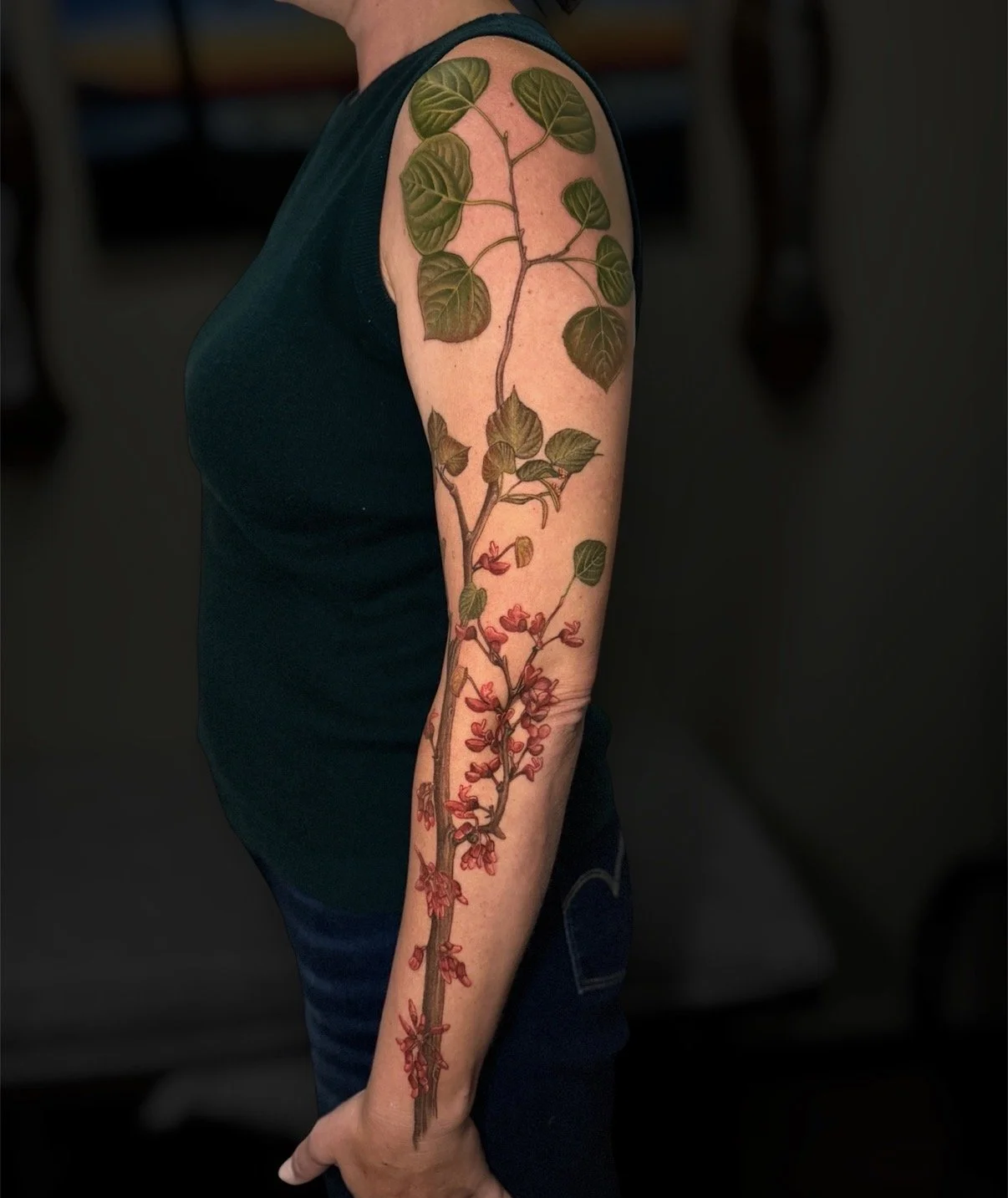 Colour botanical sleeve tattoo with large green leaves and pink blossoms along branching stems, by Chris Kennedy.