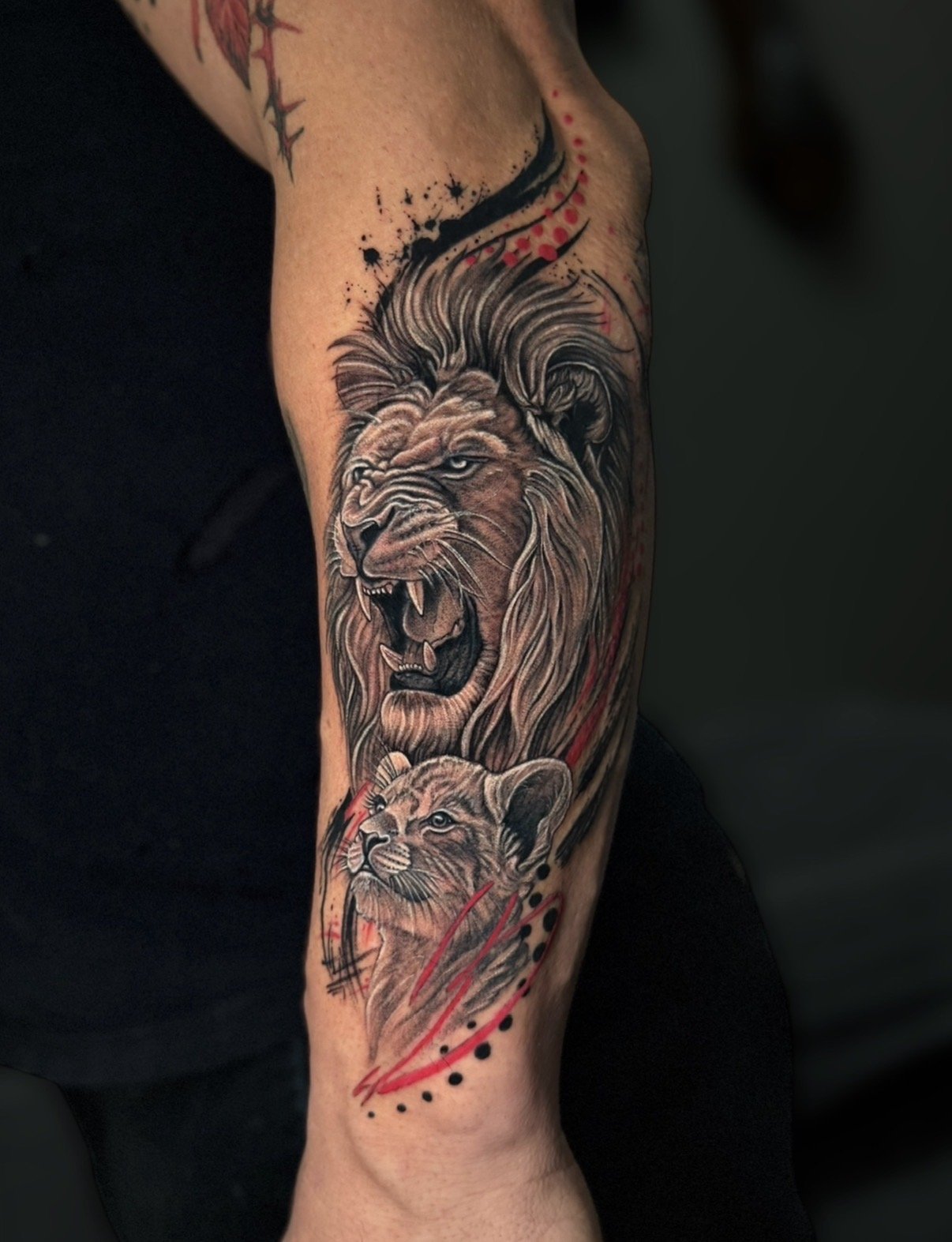 Black and grey lion and cub tattoo with red accents, by Chris Kennedy.