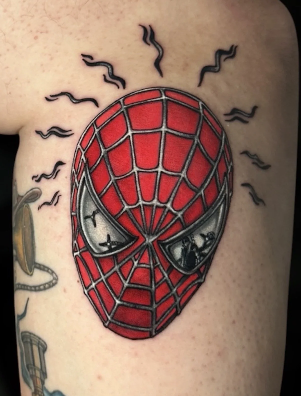 Colour Spider-Man mask tattoo with a red web pattern and black spider-sense marks, by Chris Kennedy.