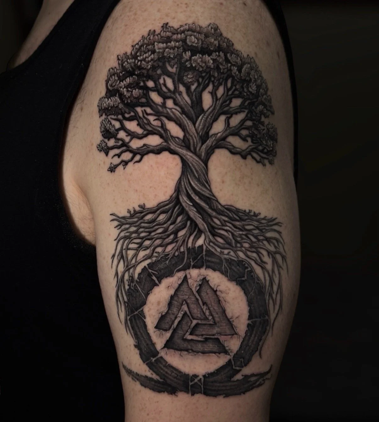 Black and grey tree tattoo with roots above a geometric symbol, by Chris Kennedy.