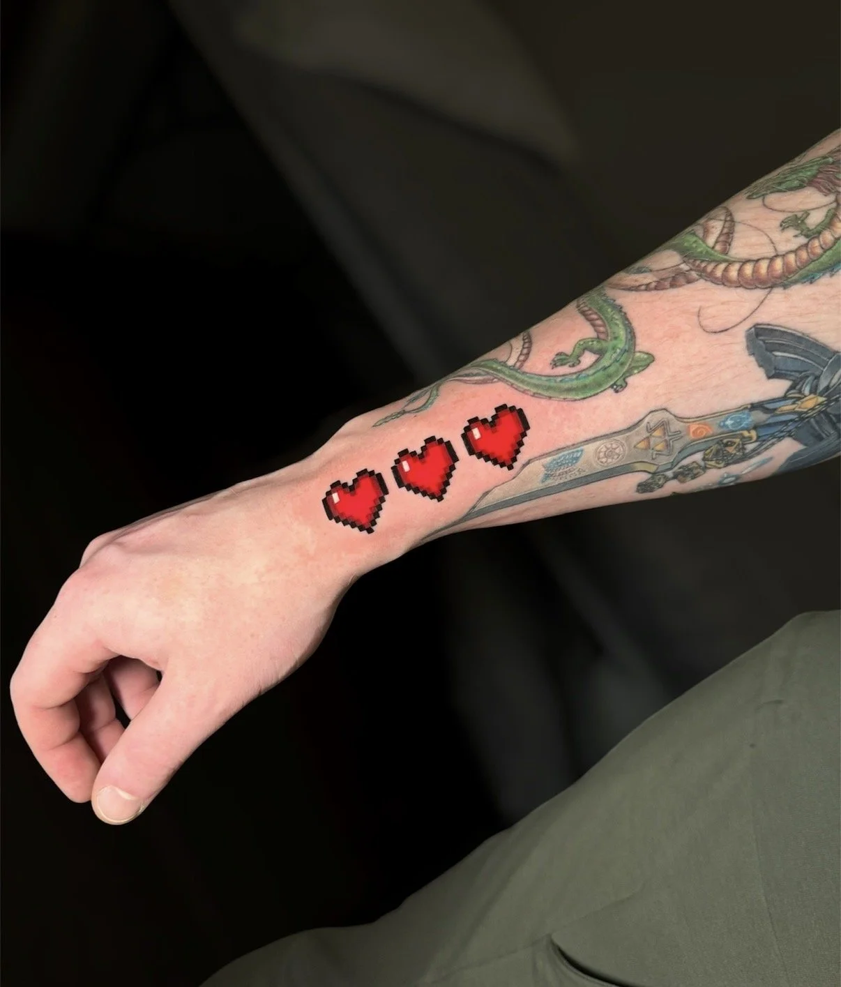 Colour tattoo of three red pixel hearts along the wrist, by Chris Kennedy.