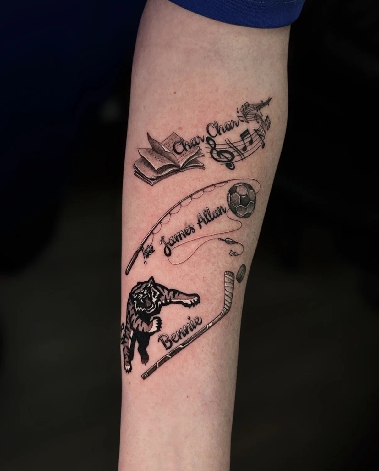 Black and grey memorial tattoo with an open book, musical notes, fishing rod, soccer ball, tiger and hockey stick, by Chris Kennedy.