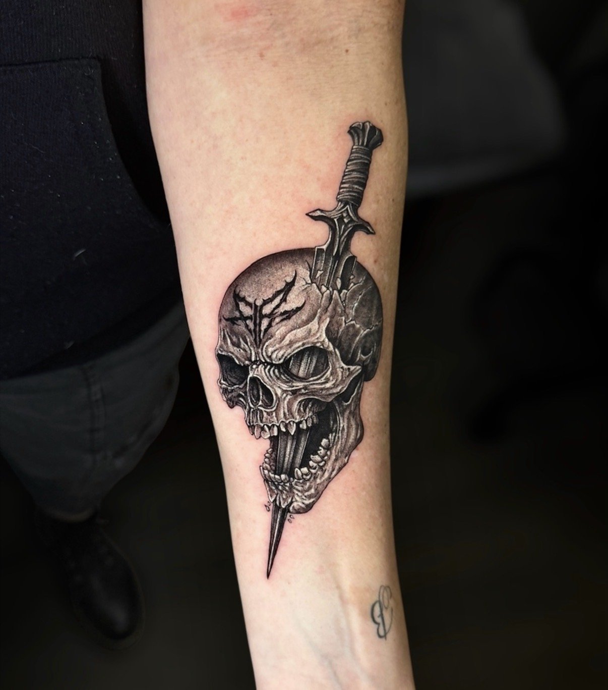 Black and grey skull tattoo pierced by a dagger, by Chris Kennedy.