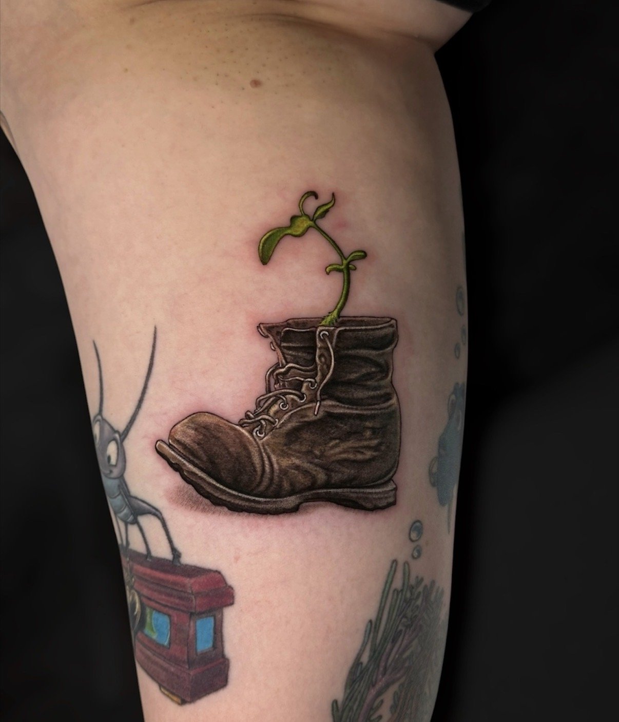 Colour tattoo of a worn brown boot with a small green plant growing from it, by Chris Kennedy.