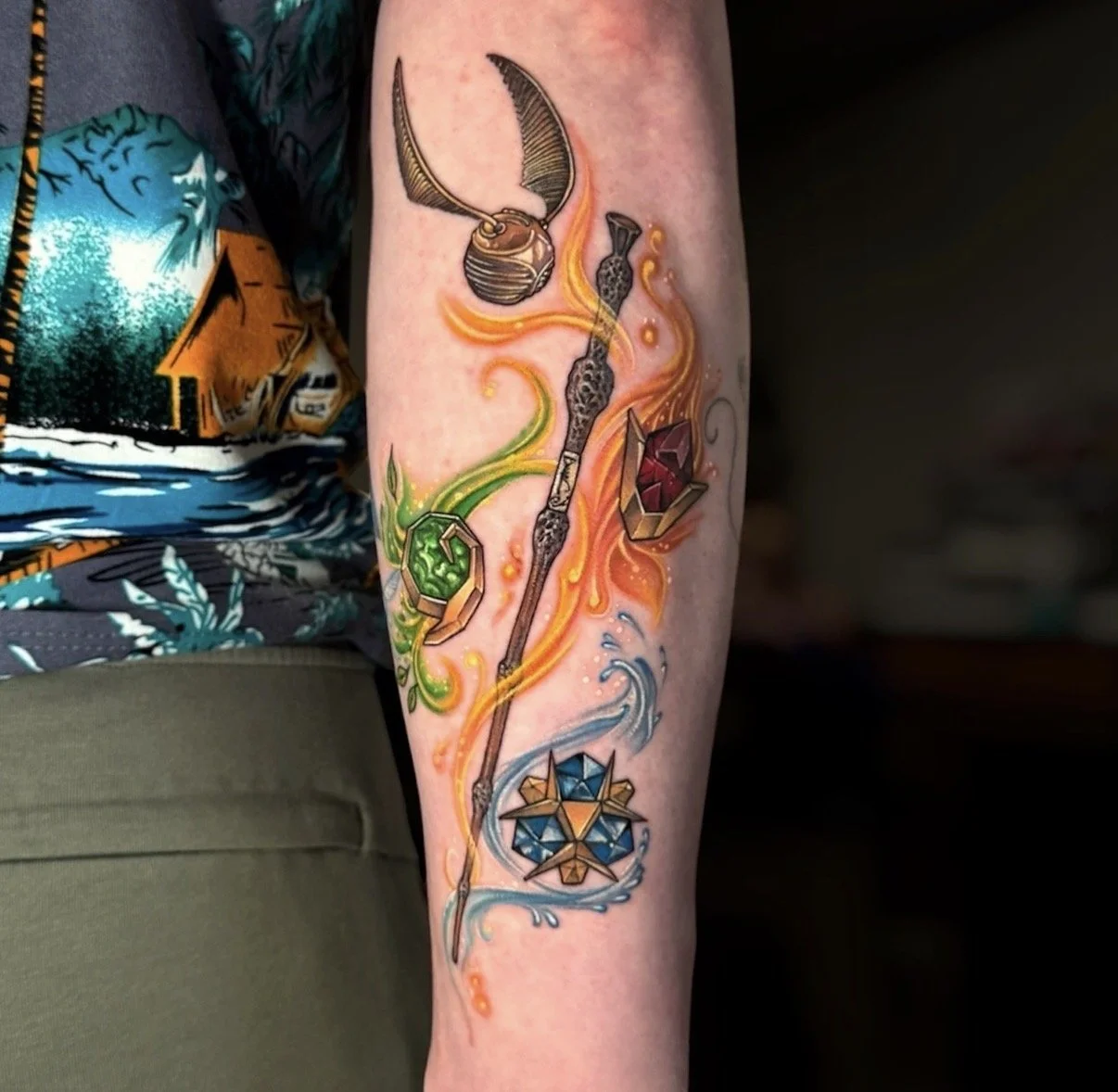 Colour magical wand tattoo with a winged golden ball, gemstones and orange, green and blue flowing accents, by Chris Kennedy.