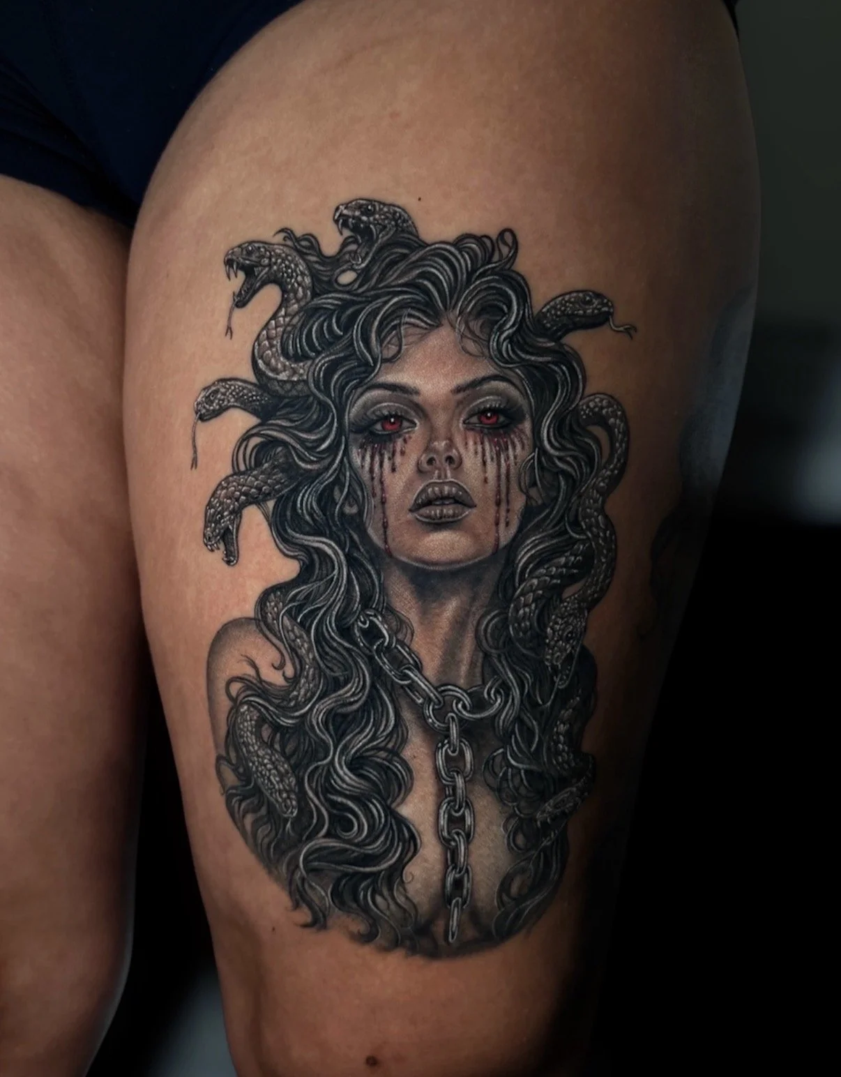 Black and grey Medusa portrait tattoo with snakes, flowing hair, a chain and red eyes and tears, by Chris Kennedy.