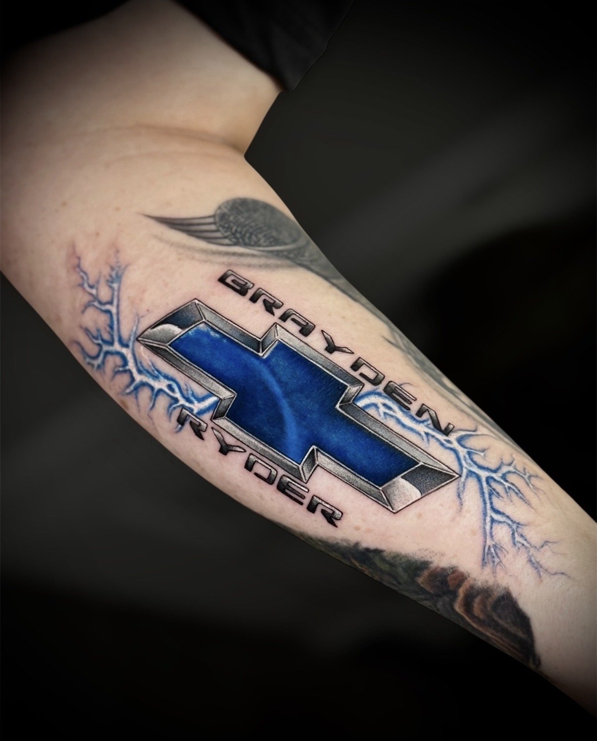 Colour blue Chevrolet emblem tattoo with lightning and the names Brayden and Ryder, by Chris Kennedy.
