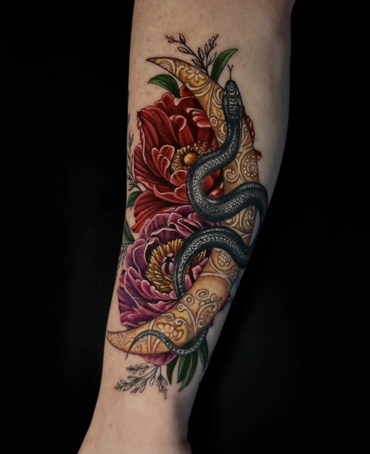 Colour snake tattoo winding around an ornate gold crescent moon with red and purple flowers, by Chris Kennedy.