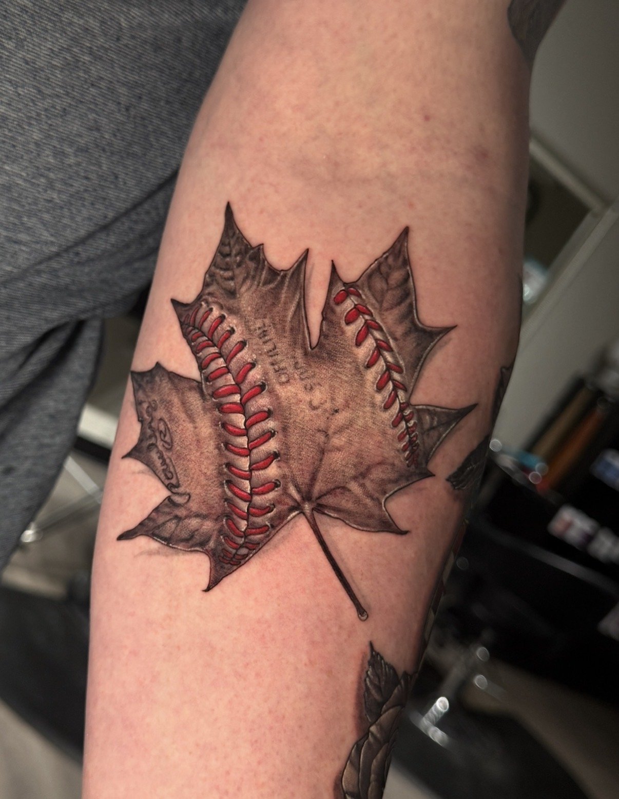 Maple leaf tattoo with baseball stitching and red details, by Chris Kennedy.