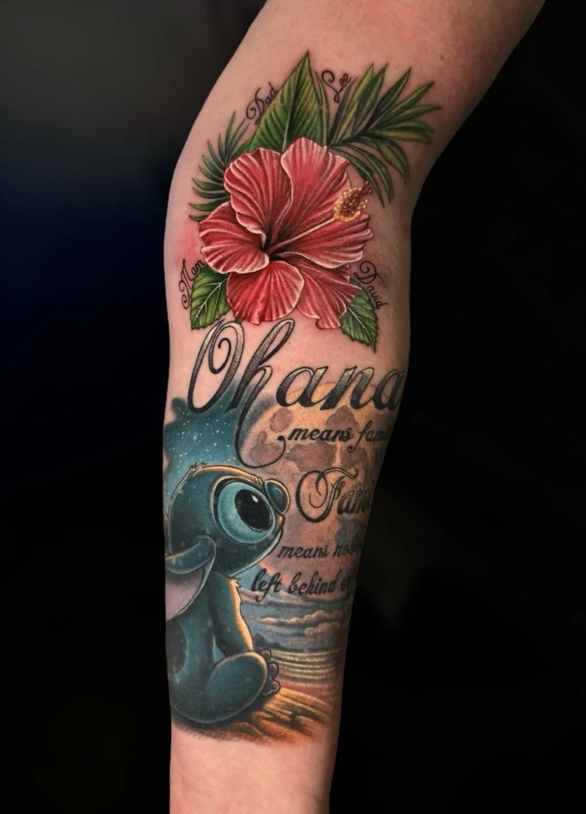 Red hibiscus flower tattoo with green leaves and a blue Stitch character, by Chris Kennedy.