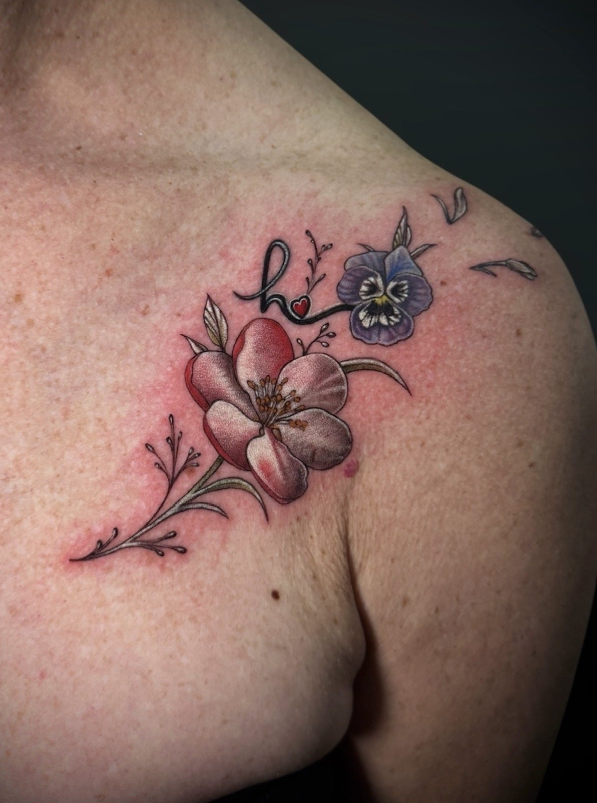 Colour floral shoulder tattoo with pink blossoms, a purple pansy and a small red heart, by Chris Kennedy.