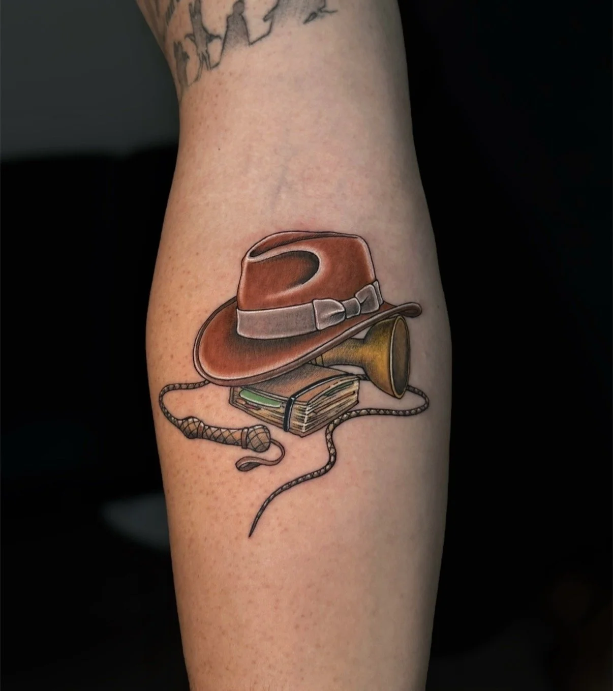 Colour Indiana Jones tattoo with a fedora, whip, journal and golden cup, by Chris Kennedy.