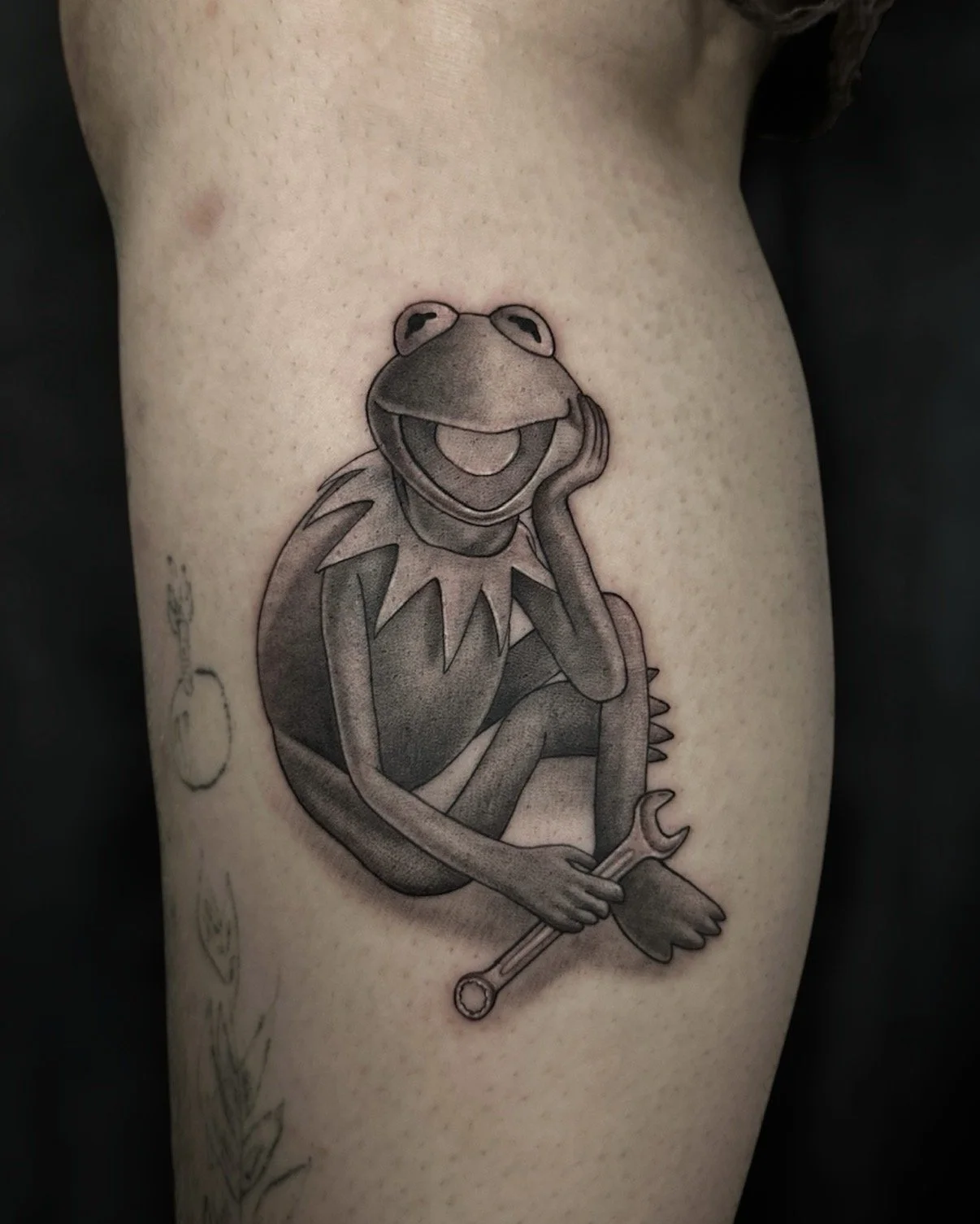 Black and grey Kermit the Frog tattoo holding a wrench, by Chris Kennedy.