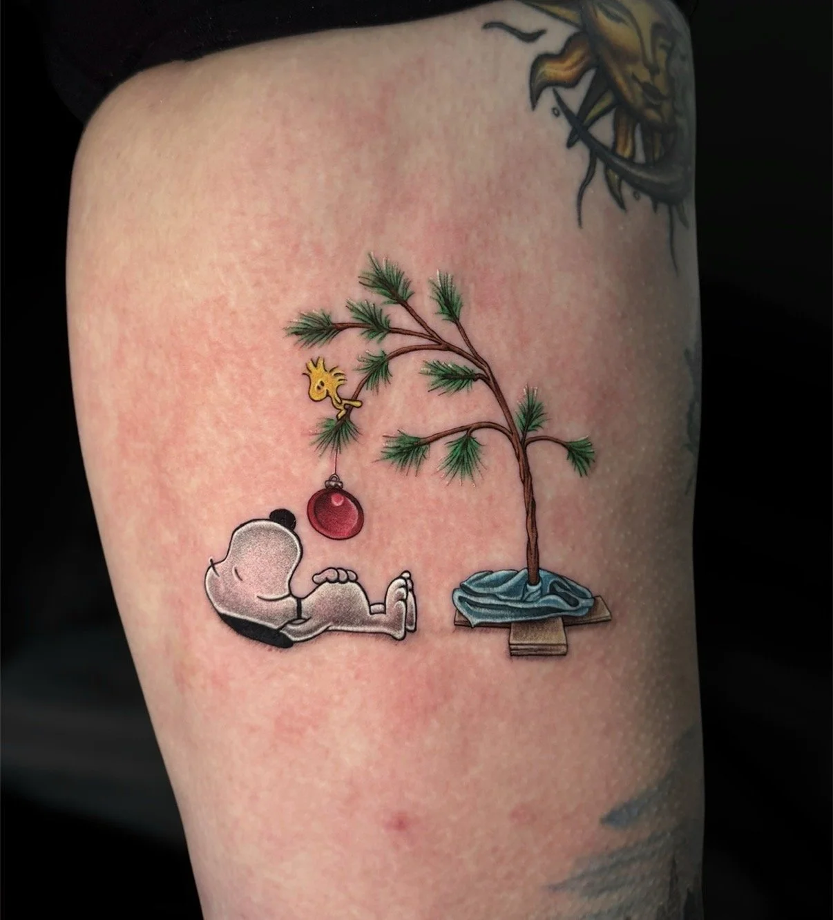 Colour Snoopy and Woodstock tattoo beside a Christmas tree with a red ornament, by Chris Kennedy.