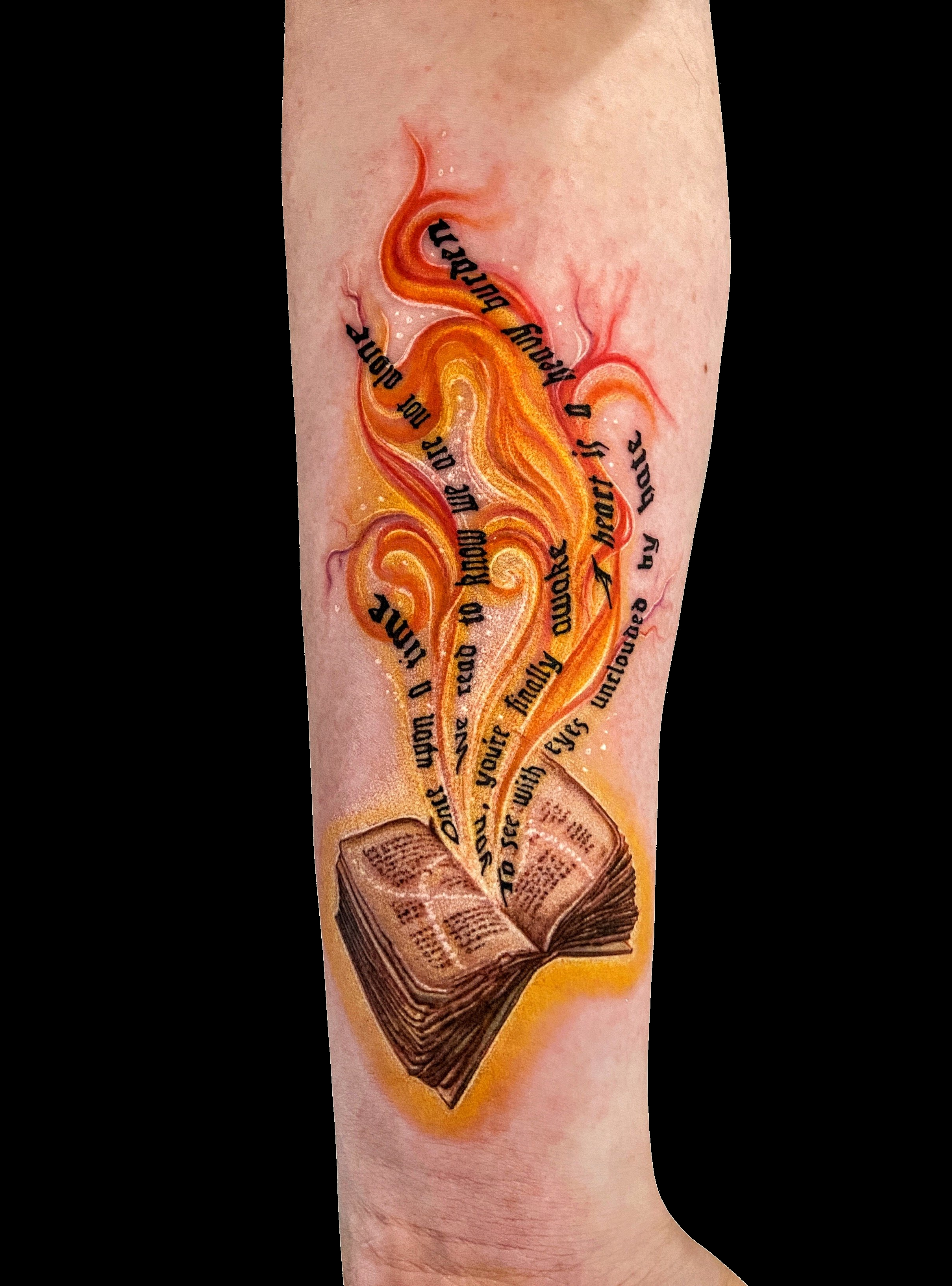 Open book tattoo with colourful birds and flowing orange accents.