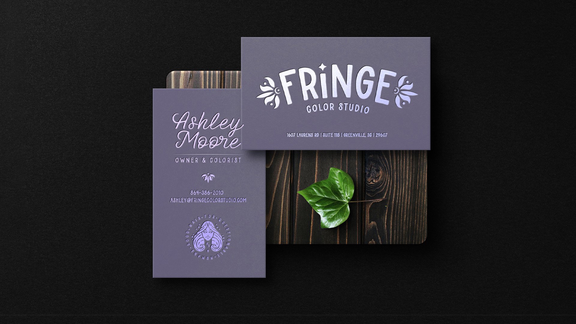 Business cards for Fringe Color Studio featuring purple backgrounds, with one card displaying the business name and logo, and the other with the owner’s name, title, contact information, and an illustration of a woman with wavy hair, all on a dark surface with a green leaf.