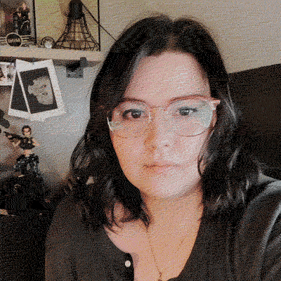 Alex Lucas, founder and owner of Oh The Raven Studio. She's a woman with shoulder-length dark hair, glasses, and a black top taking a selfie indoors.