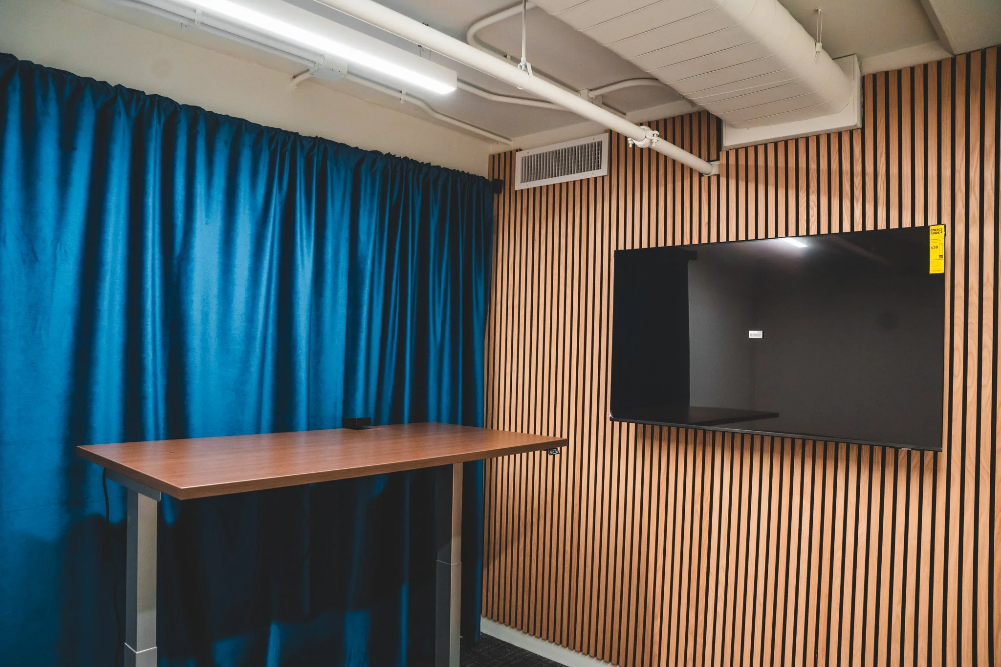 Empty room with a wooden table, blue curtains, and a black TV mounted on a wall with wooden slats.
