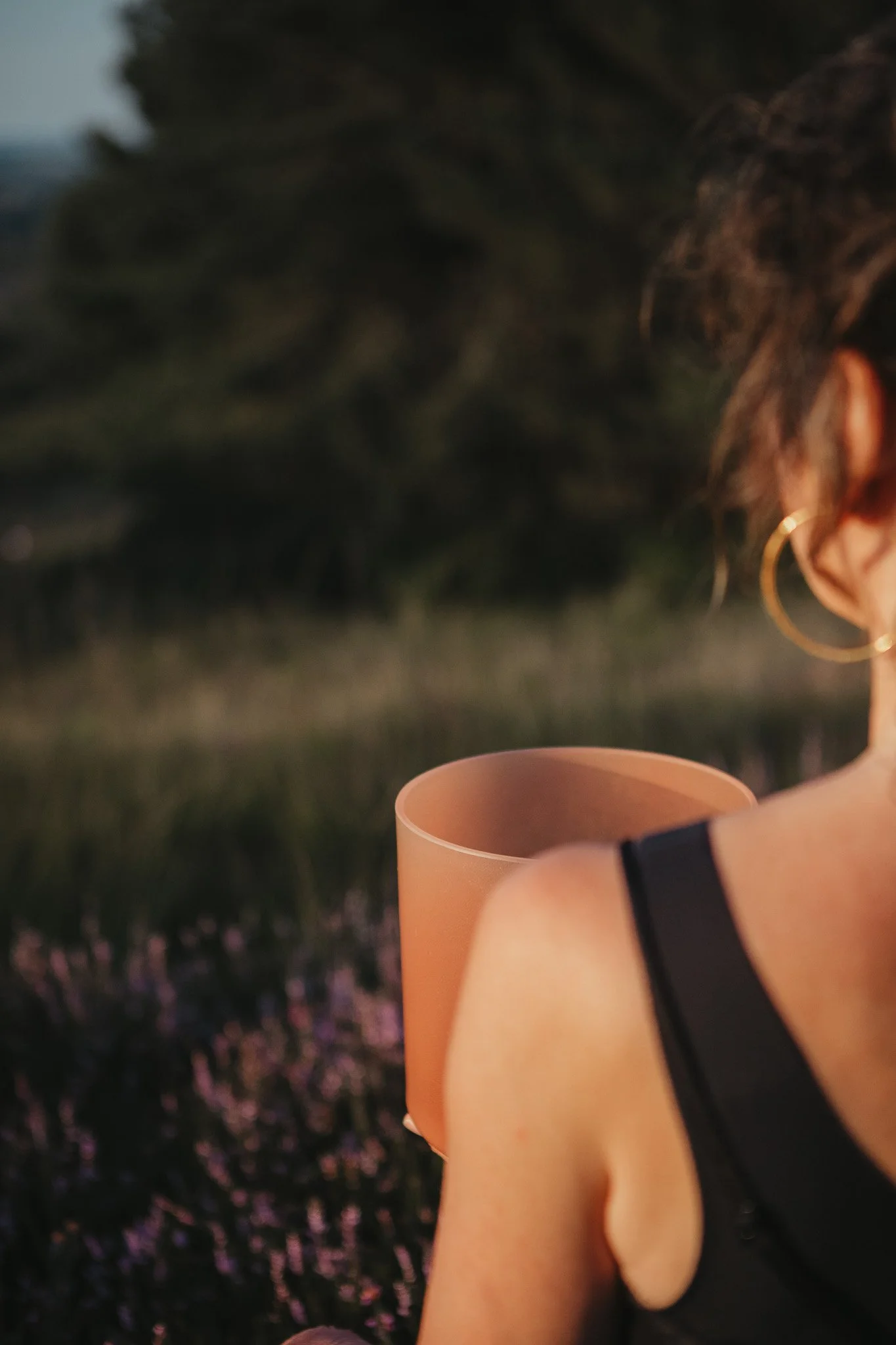 Tiffany Keywood smiling and holding a alchemy crystal signing bowl outdoors in a natural setting with greenery and trees in the background.