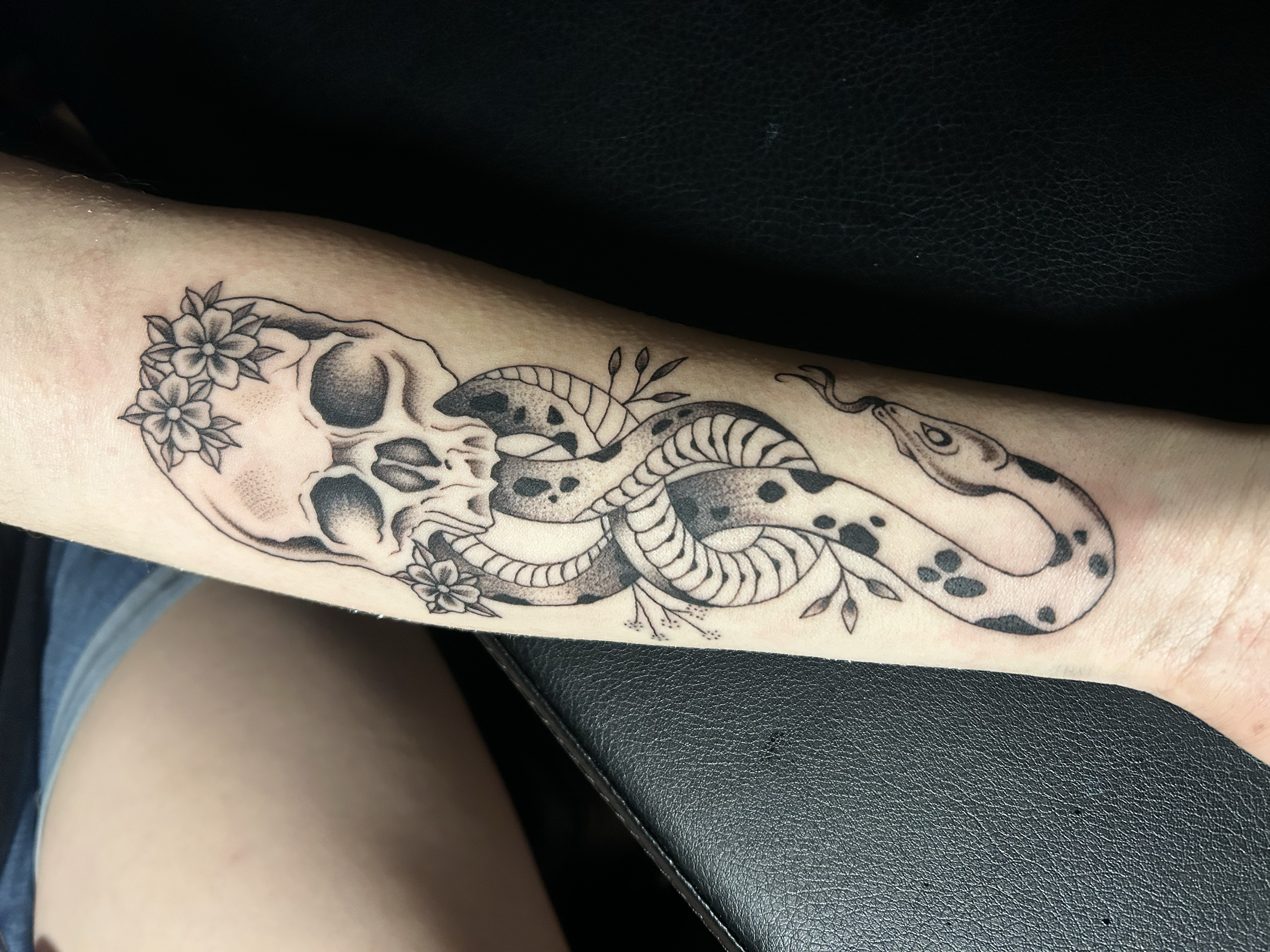 Tattoo of a human skull with flowers around it and a snake weaving through the skull and flowers.